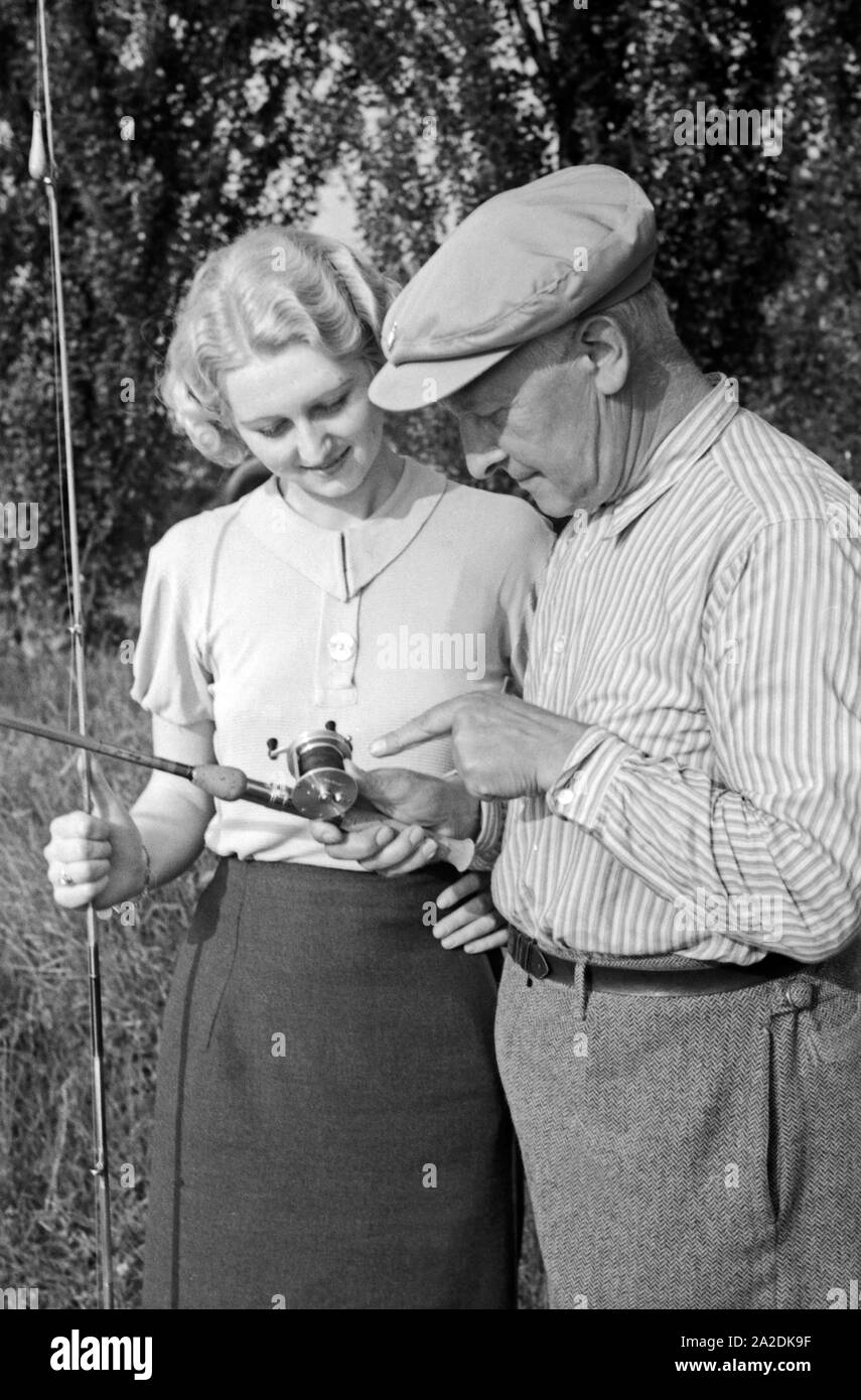 Eine Frau hört sich Tipps und Belehrungen männlicher Profi Angler eine bei einem Angelwettbewerb, Deutschland 1930er Jahre. Eine Frau, die zuhören und lernen von ihren männlichen Konkurrenten an ein Angeln Contest, Deutschland 1930. Stockfoto