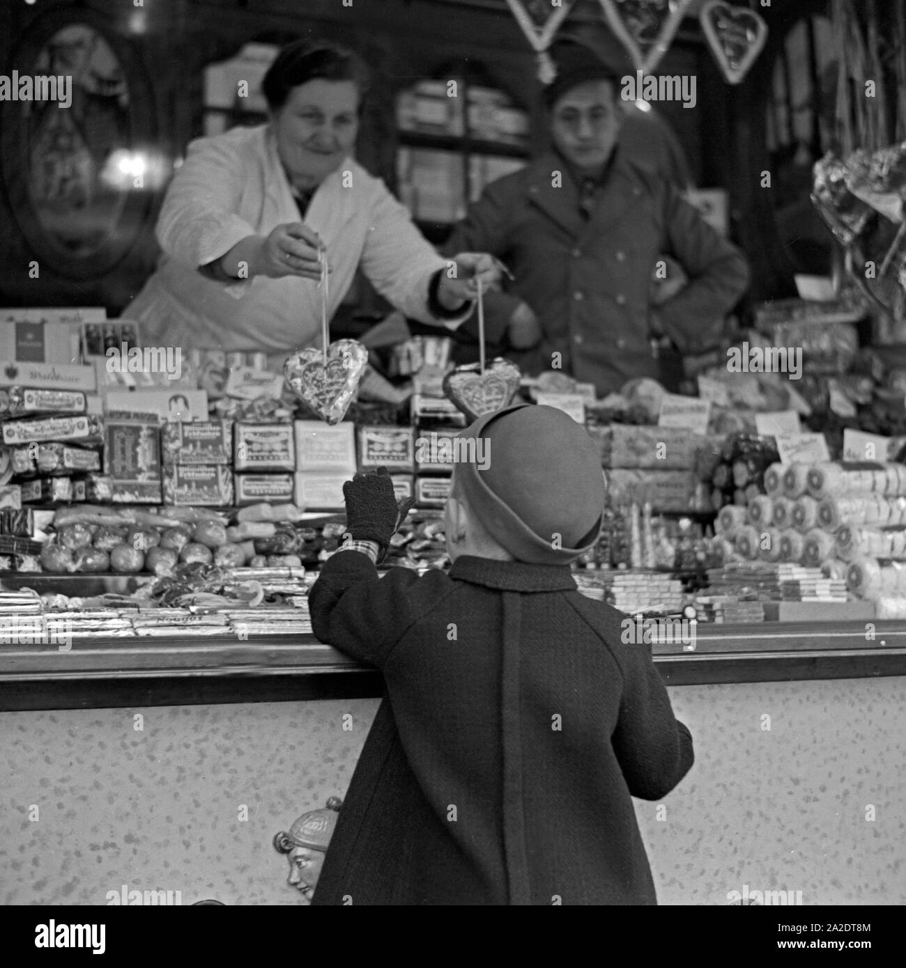 Ein kleiner Junge steht am Süßwarenstand bin Weihnnachtsmarkt, Deutschland 1930er Jahre. Ein kleiner Junge steht und das Shopping in der Süßigkeiten-Stand auf dem Weihnachtsmarkt, Deutschland 1930. Stockfoto