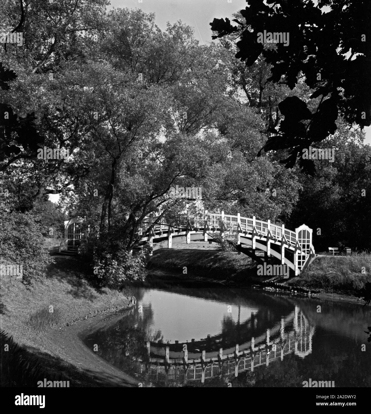 Eine kleine Brücke führt über einen Teich, nahe des Ausstellungsturms und der Stadthalle von Magdeburg, Deutschland 1930er Jahre. Eine kleine Brücke über einem Teich in der Nähe der Ausstellung Turm und der Stadthalle Halle Magdeburg, Deutschland 1930. Stockfoto