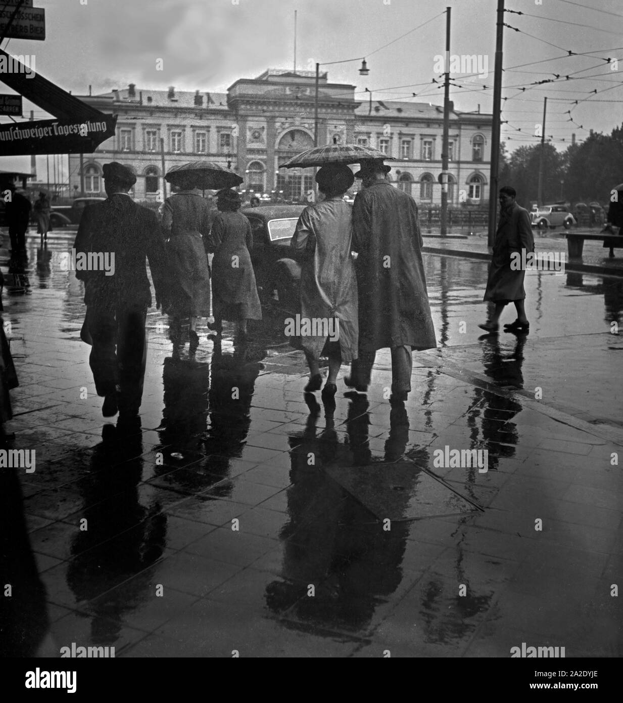 Menschen eilen im Regen auf dem Platz vor dem Hauptbahnhof in Braunschweig, Deutschland 1930er Jahre. Menschen in Eile auf dem Platz vor dem Hauptbahnhof Braunschweig, Deutschland 1930. Stockfoto