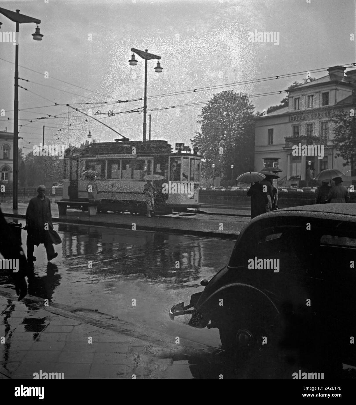 Passanten eilen im Regen über die Straße zur Straßenbahn in Braunschweig, Deutschand 1930er Jahre. Menschen über die Straße auf die Straßenbahn hetzen an verregneten Braunschweig, Deutschland 1930. Stockfoto