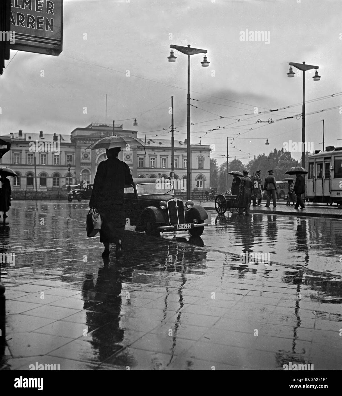 Menschen eilen im Regen auf dem Platz vor dem Hauptbahnhof in Braunschweig, Deutschland 1930er Jahre. Menschen in Eile auf dem Platz vor dem Hauptbahnhof Braunschweig, Deutschland 1930. Stockfoto