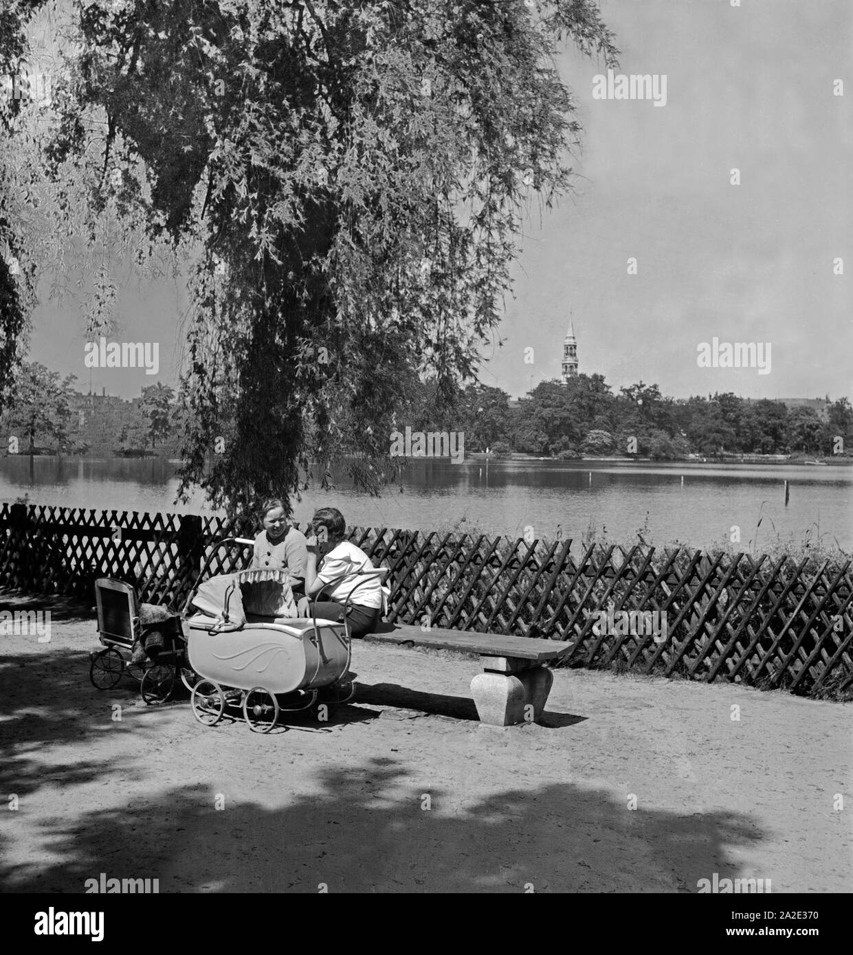 Zwei Mütter mit Kinderwagen unterhalten sich ein 1963 in einem Park in Zwickau, Deutschland 1930er Jahre. Zwei Mütter mit ihren Kinderwagen Chatten an einem See in einem Park in Zwickau, Deutschland 1930. Stockfoto
