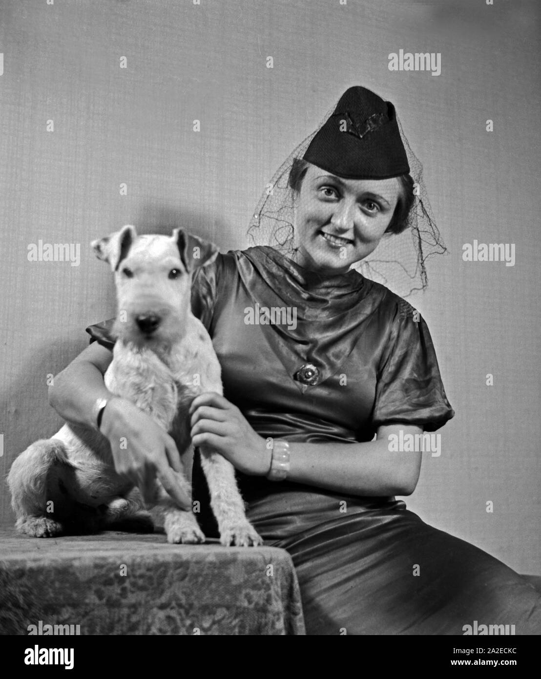 Eine Dame mit Hund im Fotostudio in zeitgenössischer Mode, Deutschland 1930er Jahre. Eine Frau und ihr Hund Haustier auf dem Foto Studio in der zeitgenössischen Mode, Deutschland 1930. Stockfoto