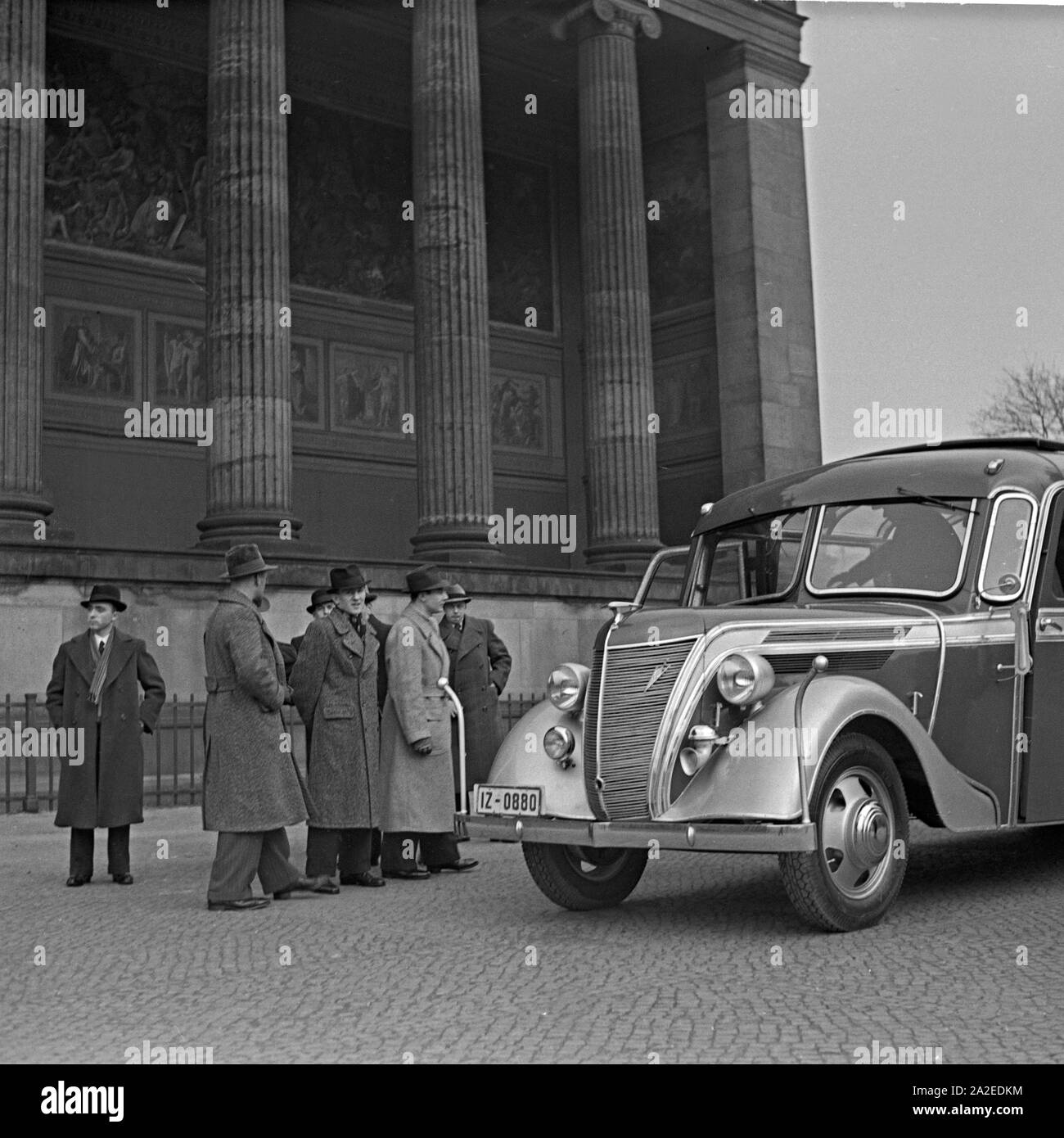 Eine Reisegruppe mit ihrem Bus vor der historischen Säulenportal, Deutschland 1930er Jahre. Eine Gruppe von Reisenden mit ihrem Trainer vor einem Gebäude mit Säulen, Deutschland 1930. Stockfoto