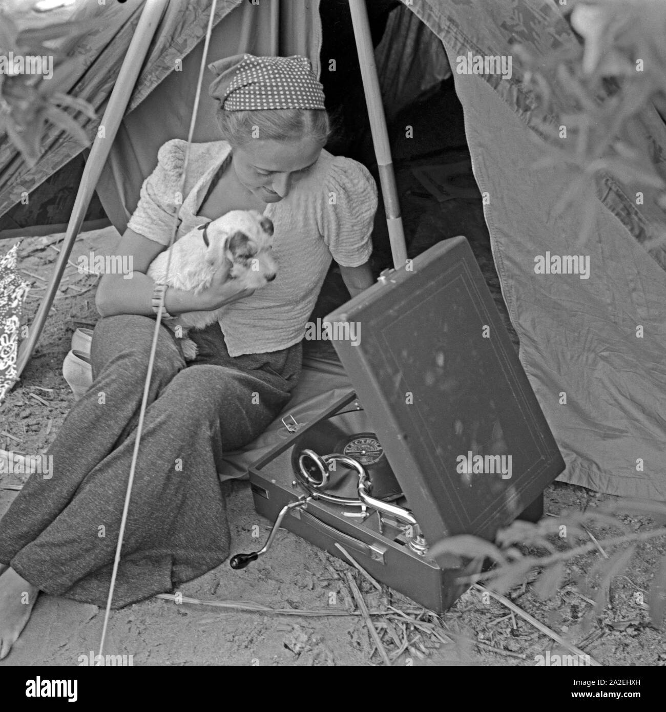 Werbefoto für Klepper Zelt: Getreu dem Werbeslogan Fahre fröhlich in die weite Welt, mit Klepper-Mantel,-Boot-und-Zelt sitzt eine junge Frau mit einem Welpen vor einem Zelt, Deutschland 1930er Jahre. Werbung für ein Klepper Zelt: Eine junge Frau sitzt mit einem Welpen vor einem Zelt, Deutschland 1930. Stockfoto