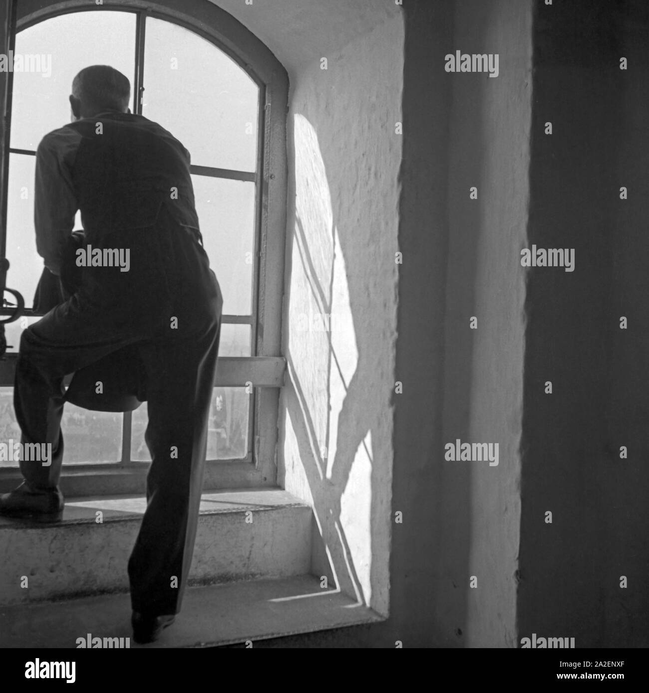 Mein Mann genießt den Ausblick auf die Stadt aus einem turmfenster der Frauenkirche in München, Deutschland 1930er Jahre. Ein Mann genießt die Aussicht über die Stadt aus einem Fenster im Glockenturm der Münchener Frauenkirche, Deutschland 1930. Stockfoto