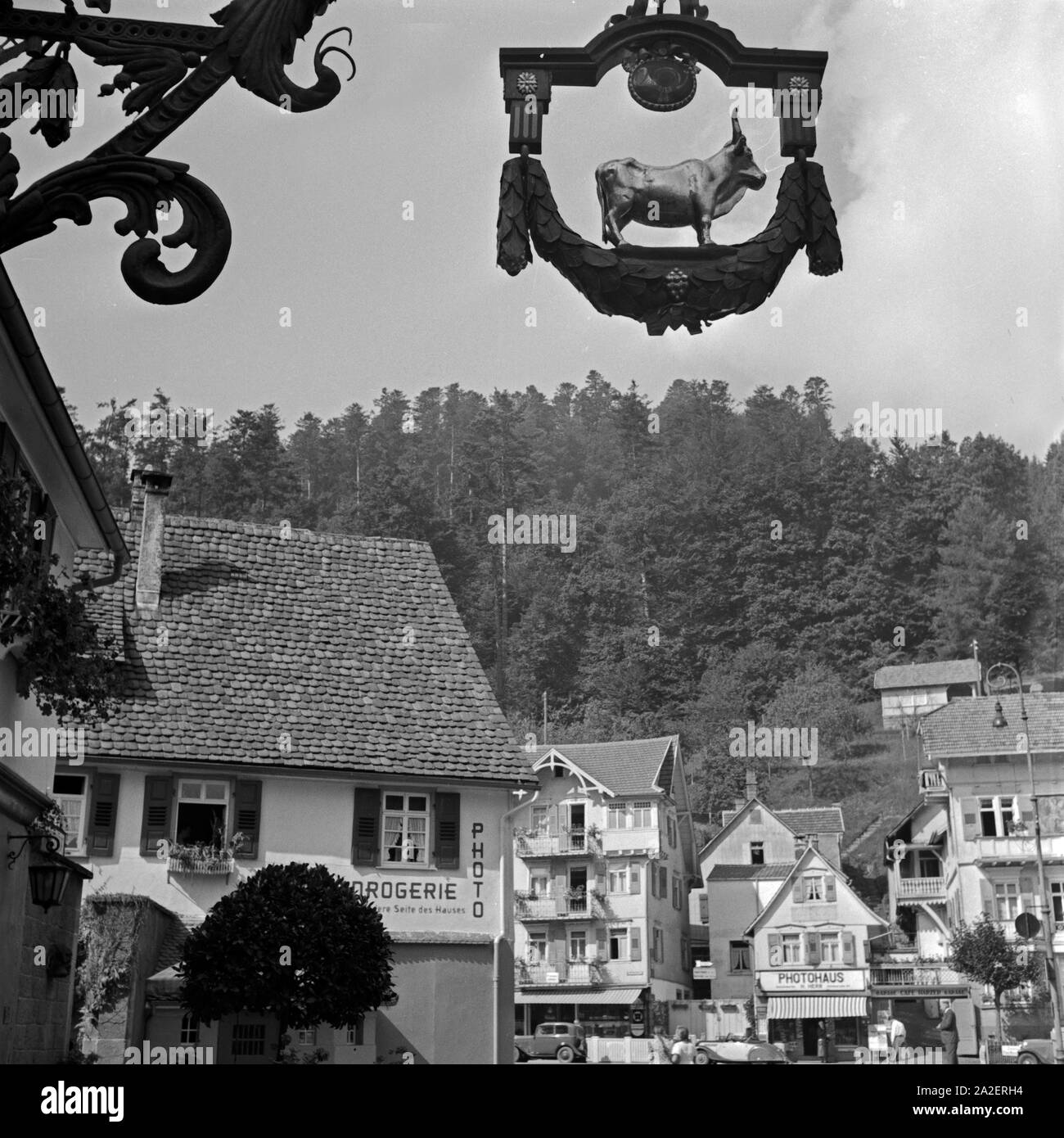 Das wirtshausschild des Gasthofs "Zum Ochsen" mit einem Blick auf Gechäfte in Herrenalb im Schwarzwald, Deutschland 1930er Jahre. Pub Zeichen der Gasthaus "Zum Ochsen" mit Blick auf die Geschäfte in Herrenalb in Schwarzwald, Deutschland 1930. Stockfoto