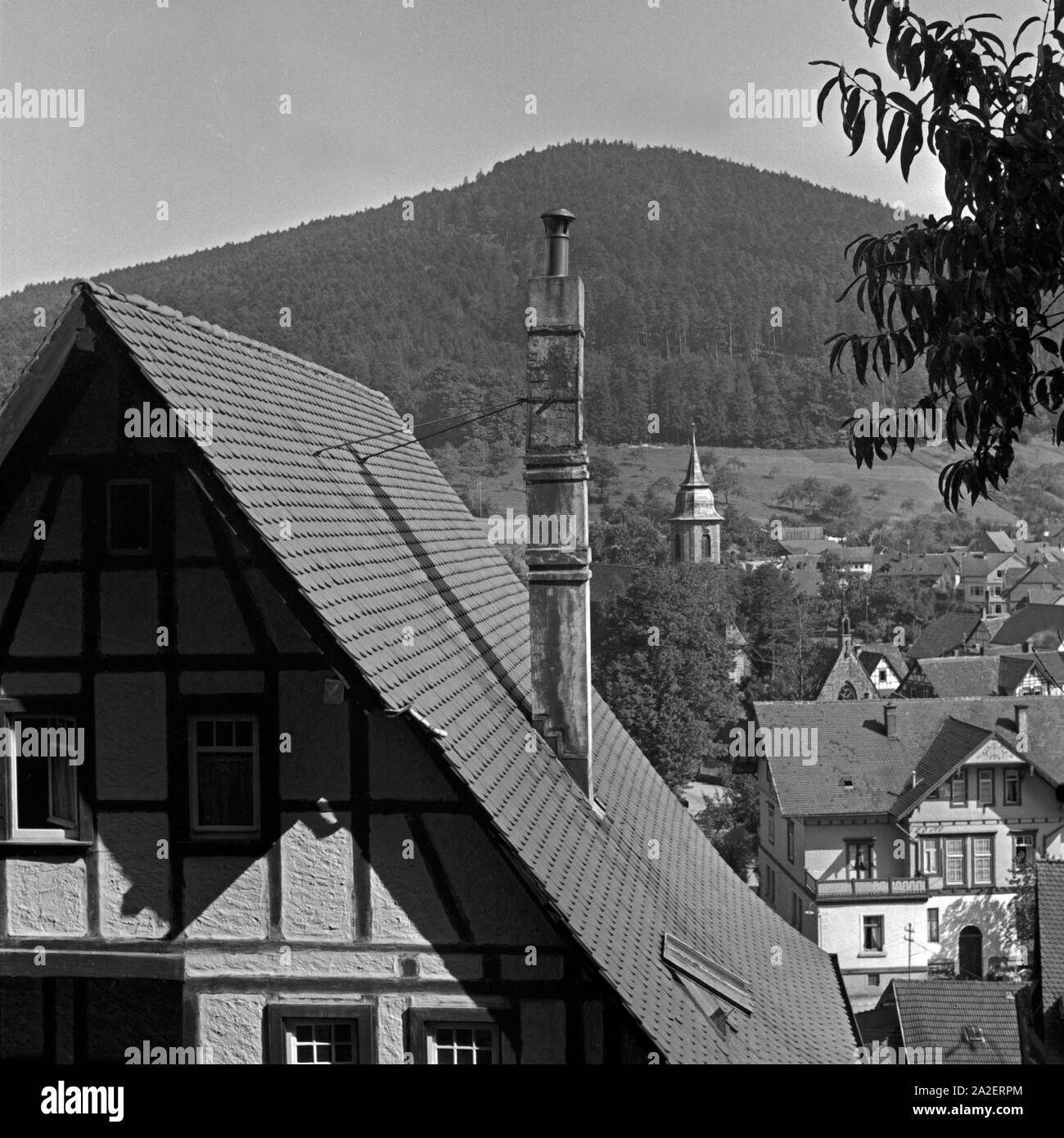 Blick auf den Turm der Klosterkirche hinter einem Fachwerkhaus in Herrenalb im Schwarzwald, Deutschland 1930er Jahre. Blick auf den Glockenturm der Klosterkirche hinter einem Fachwerkhaus in Herrenalb in Schwarzwald, Deutschland 1930. Stockfoto