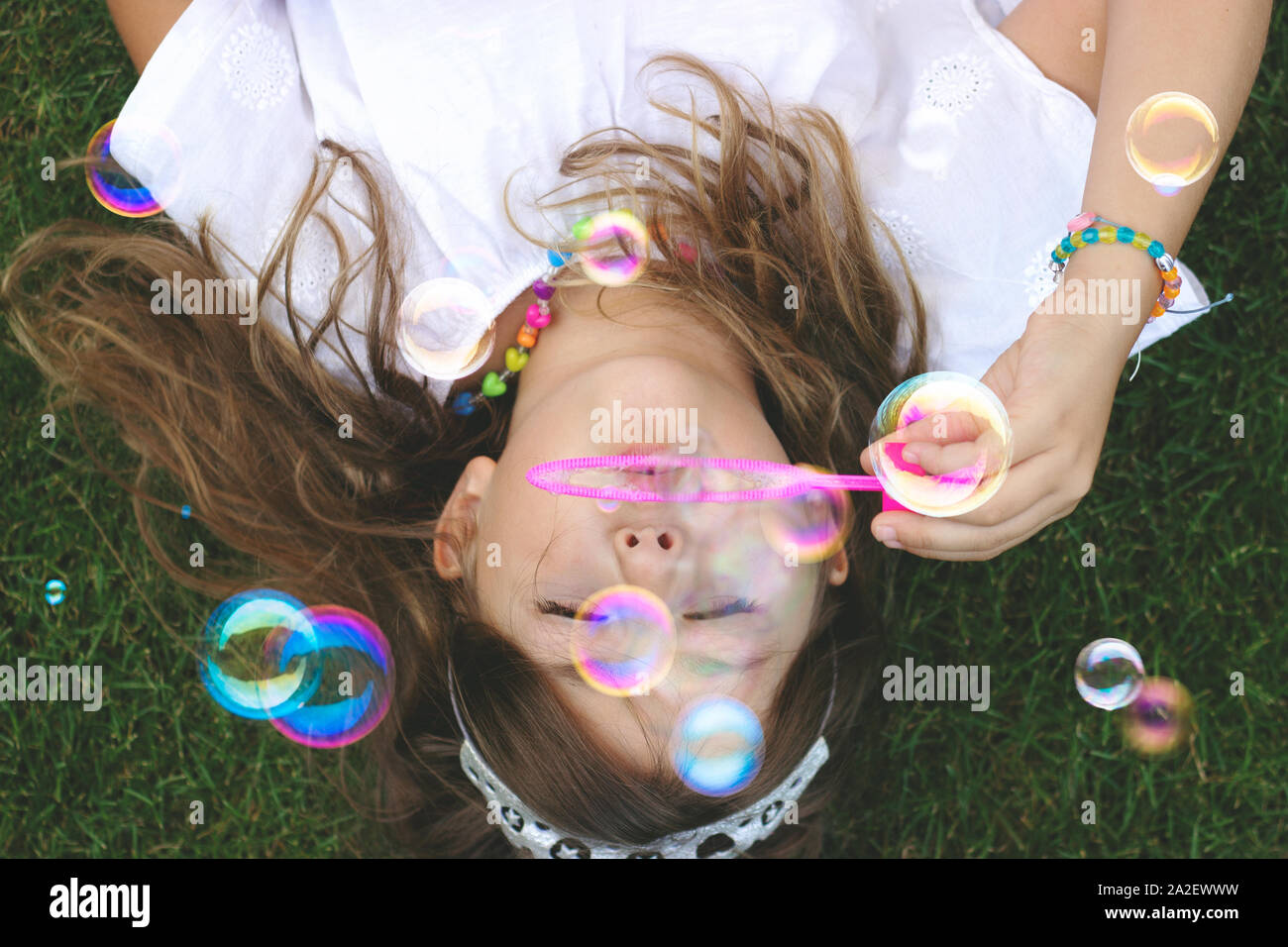 Blick von oben auf ein wunderschönes kleines Mädchen mit auf dem Gras, bläst Seifenblasen Stockfoto