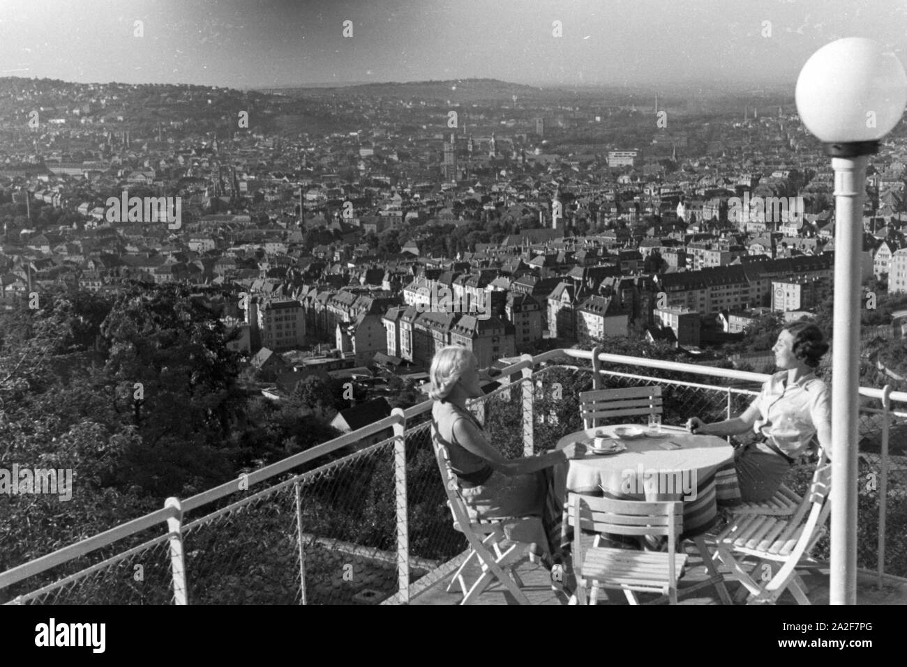 Zwei junge Frauen genießen von der Caféterrasse aus den Blick über Stuttgart, Deutschland 1930er Jahre. Zwei junge Frauen genießen Sie den Blick über Stuttgart von der Terrasse eines Cafés, Deutschland 1930. Stockfoto