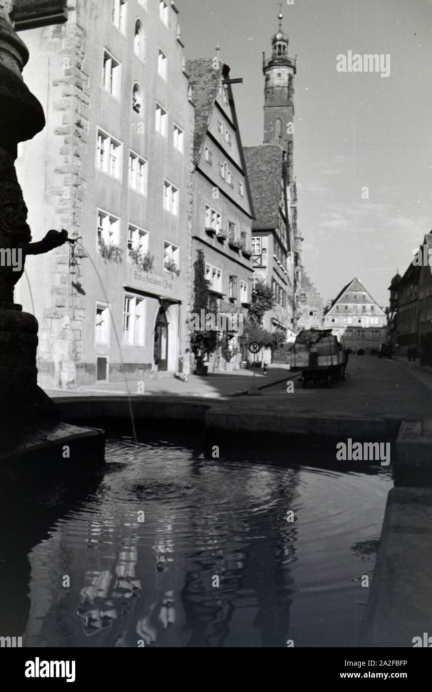 Ein Springbrunnen mit des imposanten Rathauses in Rothenburg o.d. Tauber, von dem der gotische Teil mitsamt hohem Turm im Hintergrund sichtbar ist Stockfoto