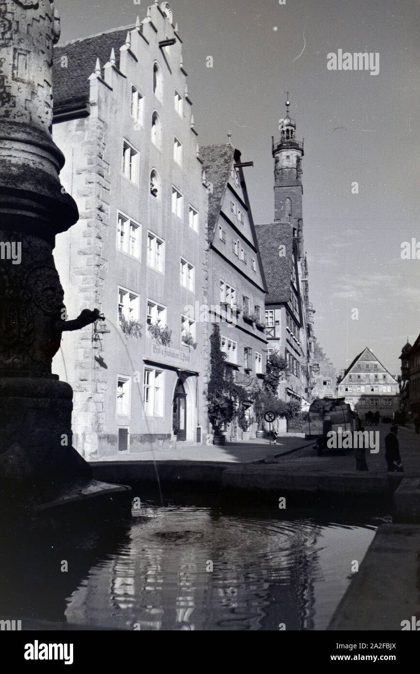Ein Springbrunnen mit des imposanten Rathauses in Rothenburg o.d. Tauber, von dem der gotische Teil mitsamt hohem Turm im Hintergrund sichtbar ist Stockfoto