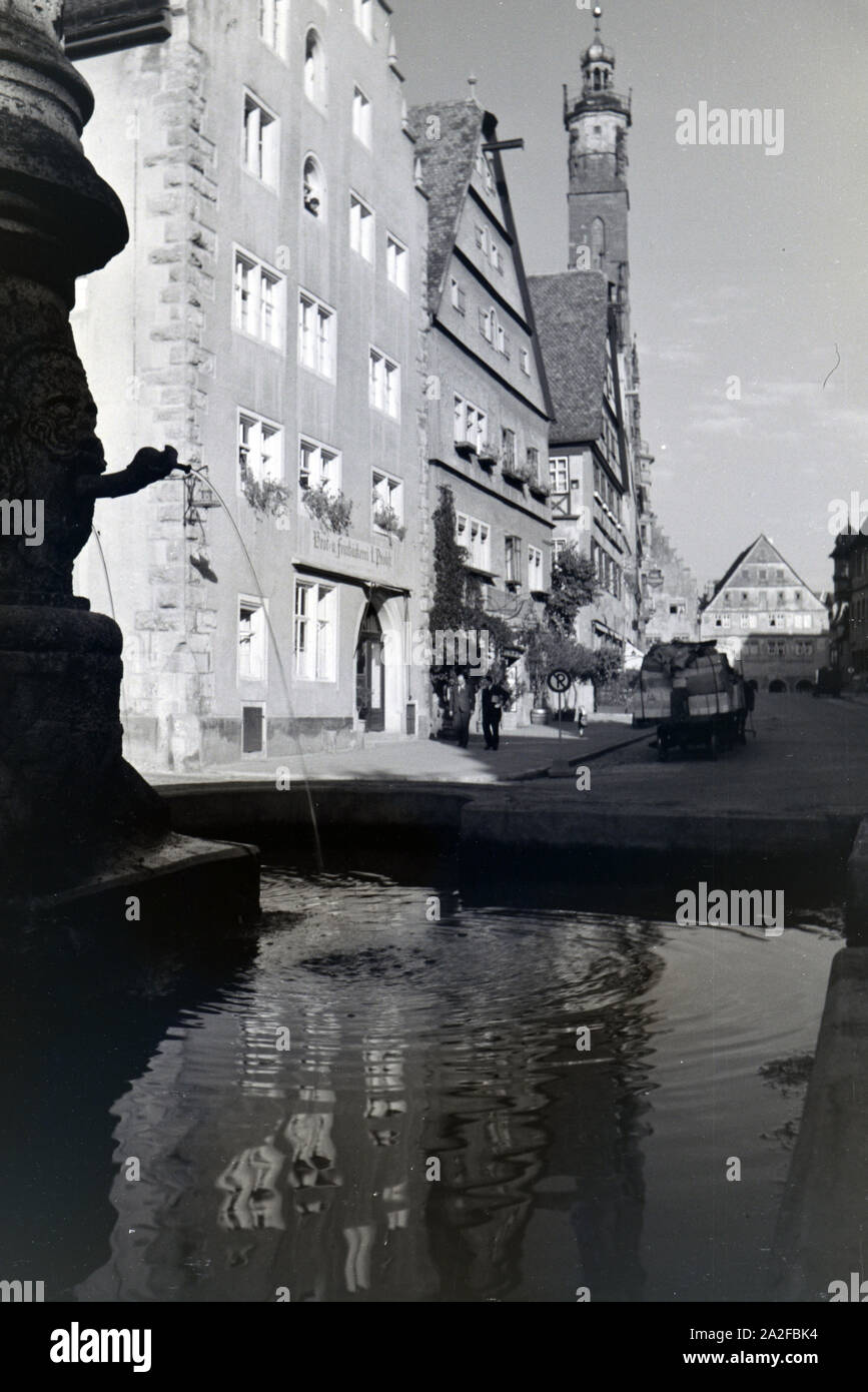 Ein Springbrunnen mit des imposanten Rathauses in Rothenburg o.d. Tauber, von dem der gotische Teil mitsamt hohem Turm im Hintergrund sichtbar ist Stockfoto