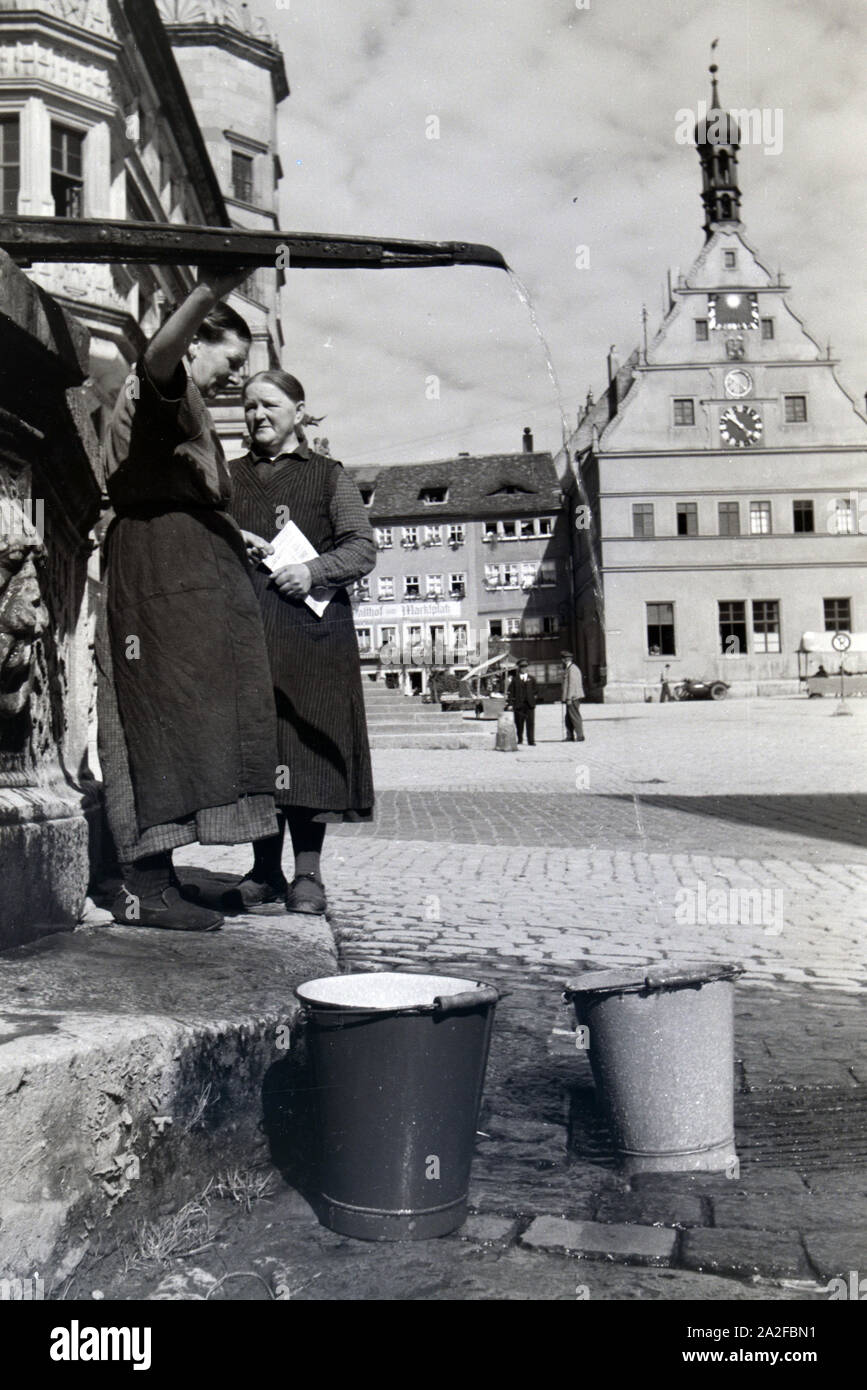 Zwei Frauen unterhalten sich über 5/6 für sie sterben Wassereimer mit Wasser aus dem Springbrunnen am Marktplatz vor dem Rathaus und der Ratstrinkstube voll laufen lassen, Rothenburg o.d. Tauber, Deutschland 1930er Jahre. Zwei Frauen in einem Chat, während die bucktes Befüllung mit Wasser aus dem Brunnen auf dem Marktplatz in der Nähe des Rathaus und Ratstrinkstube in Rothenburg o.d. Tauber, Deutschland der 1930er Jahre gelegt. Stockfoto