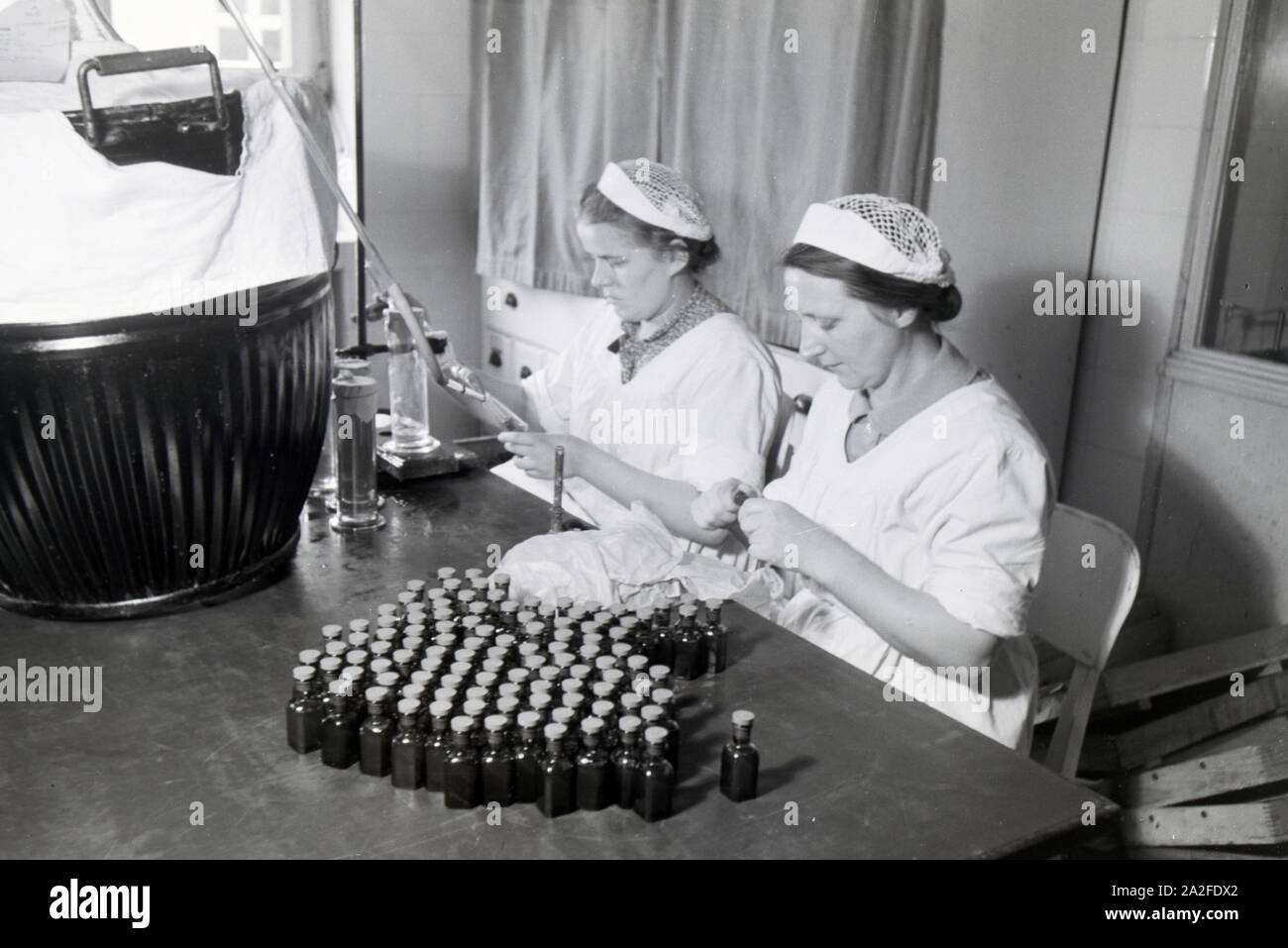 Zwei Laborantinnen füllen in Arbeit der Behringwerke Medikamente in kleine Flaschen ab, Marburg, Deutschland 1930er Jahre. Zwei lab Assistenten sind Befüllen Medikation in kleinen Flaschen im Labor der Behringwerke, Marburg, Deutschland 1930. Stockfoto