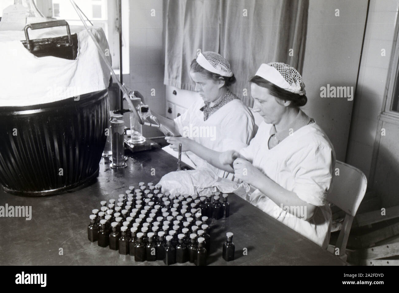 Zwei Laborantinnen füllen in Arbeit der Behringwerke Medikamente in kleine Flaschen ab, Marburg, Deutschland 1930er Jahre. Zwei lab Assistenten sind Befüllen Medikation in kleinen Flaschen im Labor der Behringwerke, Marburg, Deutschland 1930. Stockfoto