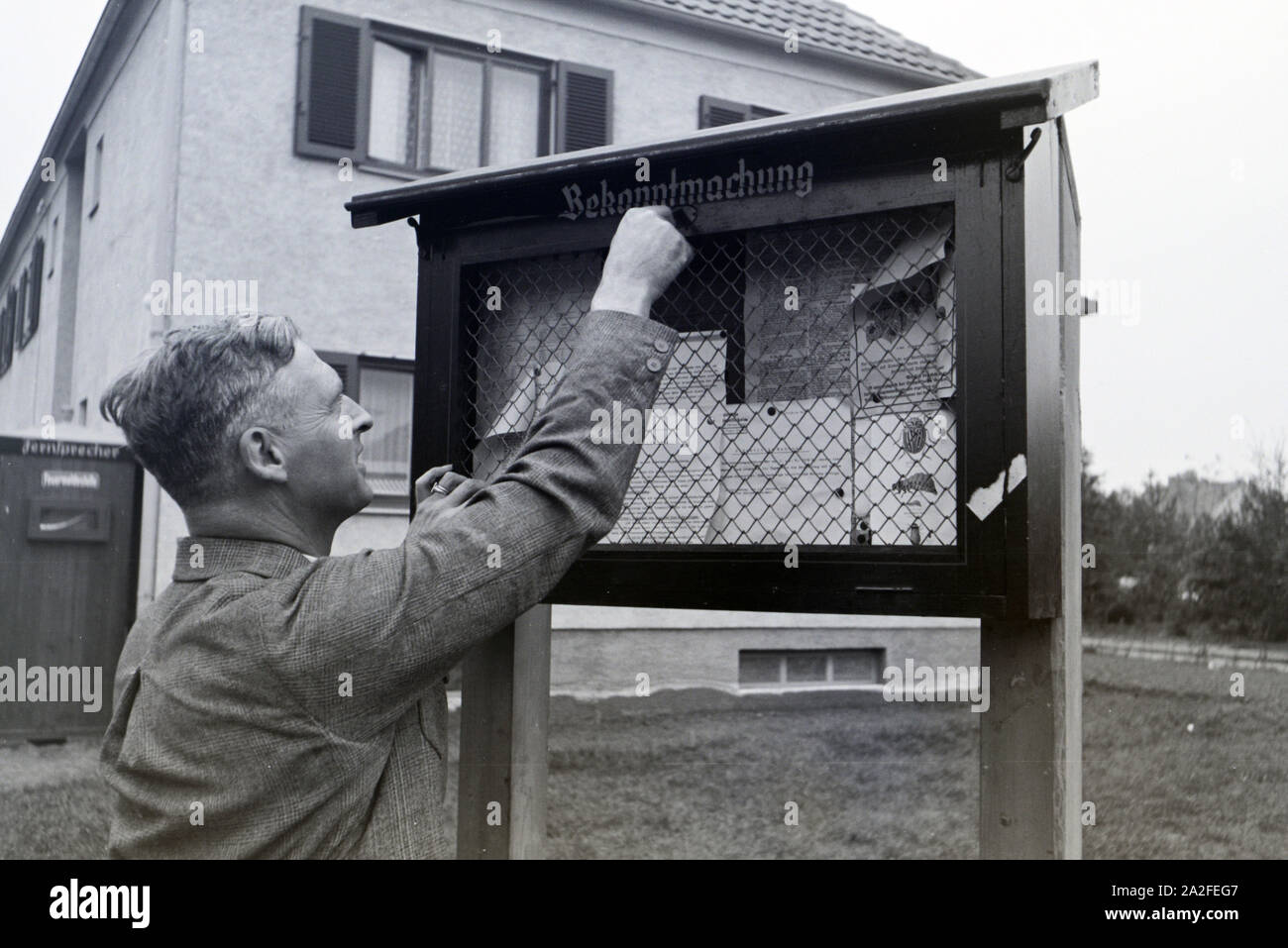 Der Zeppelinheimer Bürgermeister und Luftschiffkapitän Hans von Schiller schließt die öffentlichen Bekanntmachungstafel der Gemeinde auf, bei Frankfurt am Main, Deutschland 1930er Jahre. Der Bürgermeister von Zeppelinheim und Luftschiff captain Hans von Schillerunlocking der öffentlichen schwarzen Brett der Gemeinschaft, in der Nähe von Frankfurt am Main, Deutschland 1930er. Stockfoto