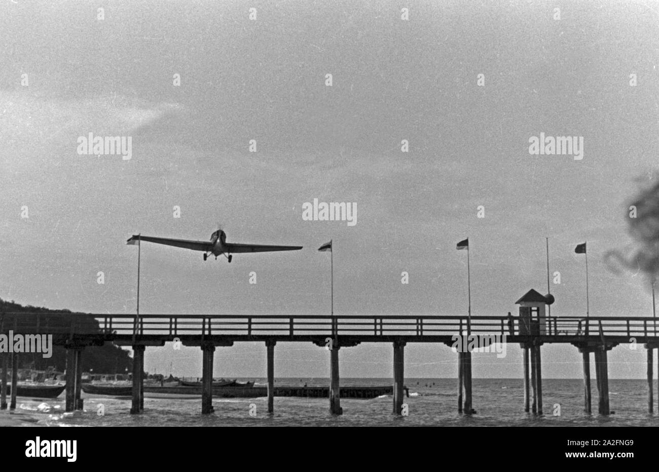 Ein Flugzeug im Tiefflug über einem Steg an der Ostsee, Deutschland 1930er Jahre. Ein Flugzeug auf einer niedrigen Ebene Flug über einen Pier an der Ostsee, Deutschland 1930. Stockfoto