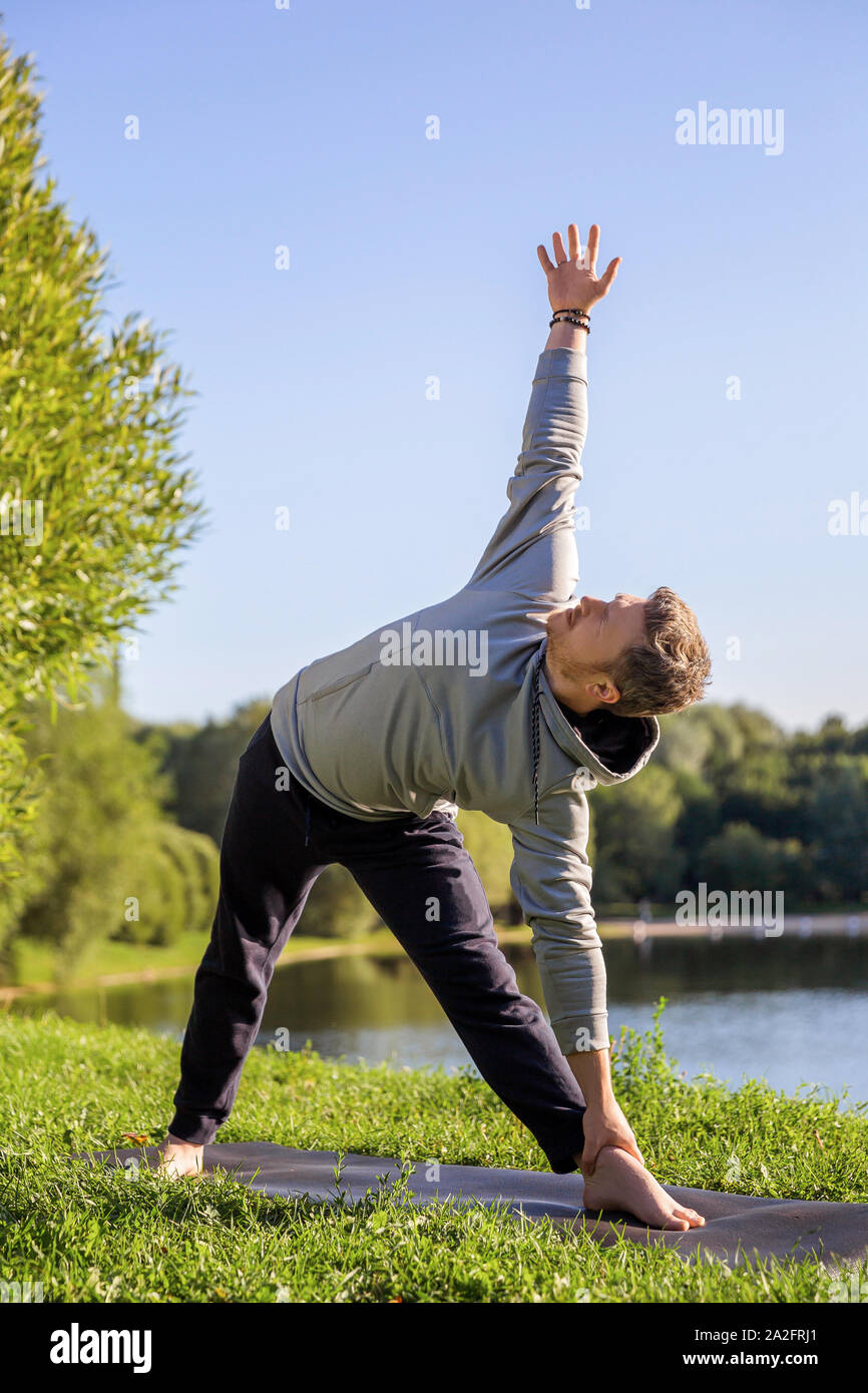 Man Yoga Asanas im City Park inspiriert. Fitness im Freien und Life Balance Konzept. Stretching. Dreieck Pose oder Trikonasana Stockfoto