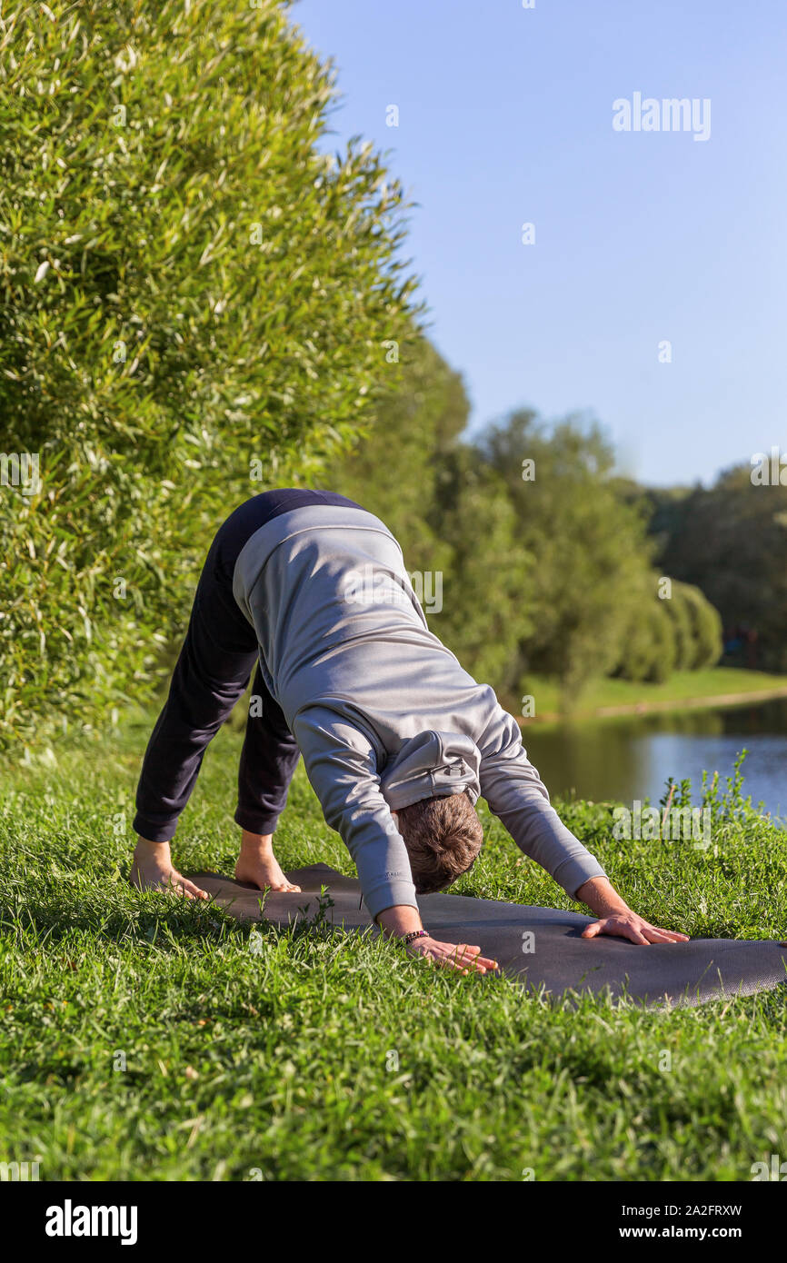 Man Yoga Asanas im City Park inspiriert. Fitness im Freien und Life Balance Konzept. In den nach unten schauenden Hund Pose oder Adho Mukha shvanasana Stockfoto