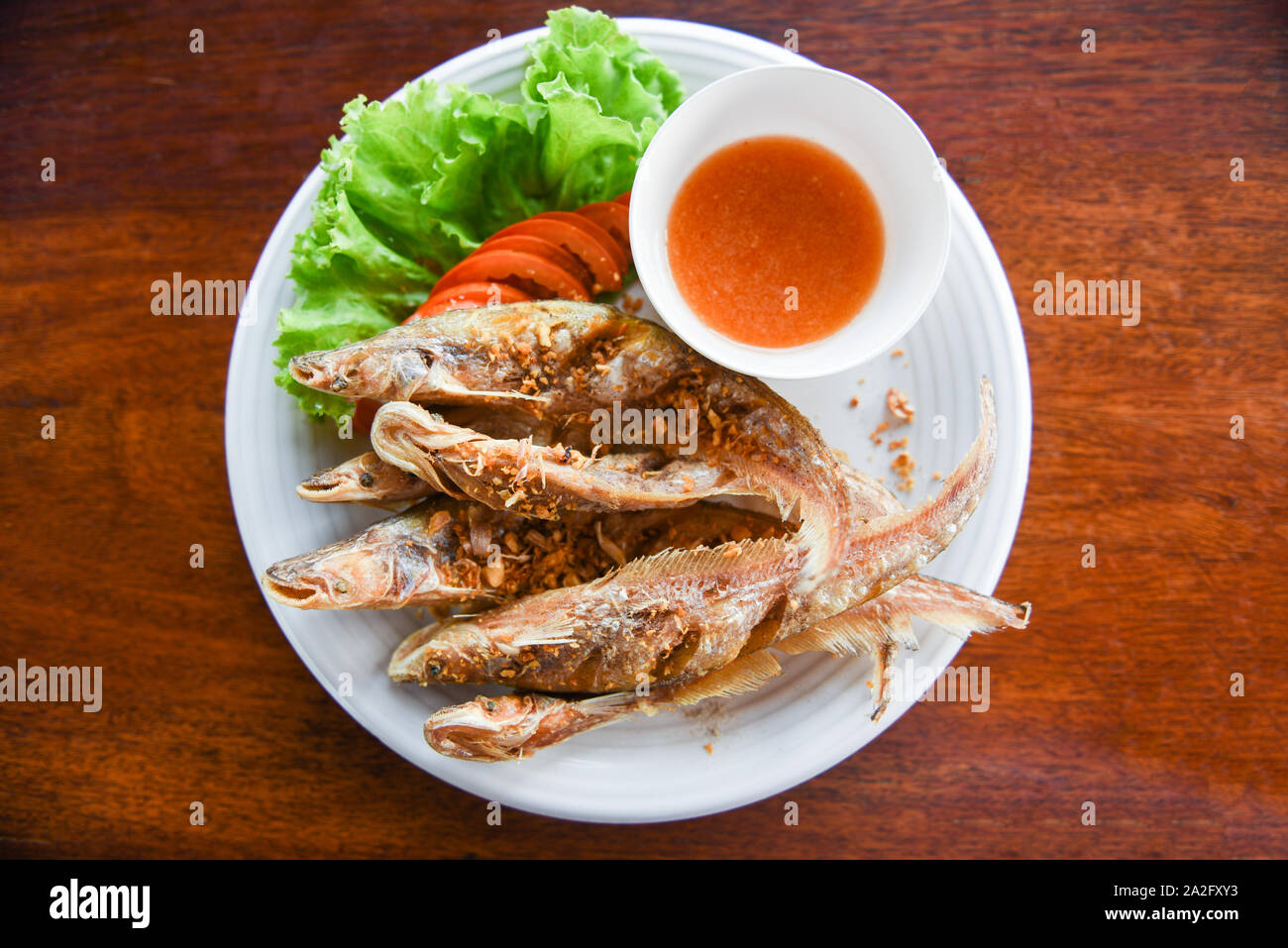 Gebratener Fisch mit Gemüse Salat Tomaten und Soße auf weiße Platte Holztisch/Süßwasserfische Mekong Andere Namen Sheatfishes Siluriformes Silur Stockfoto