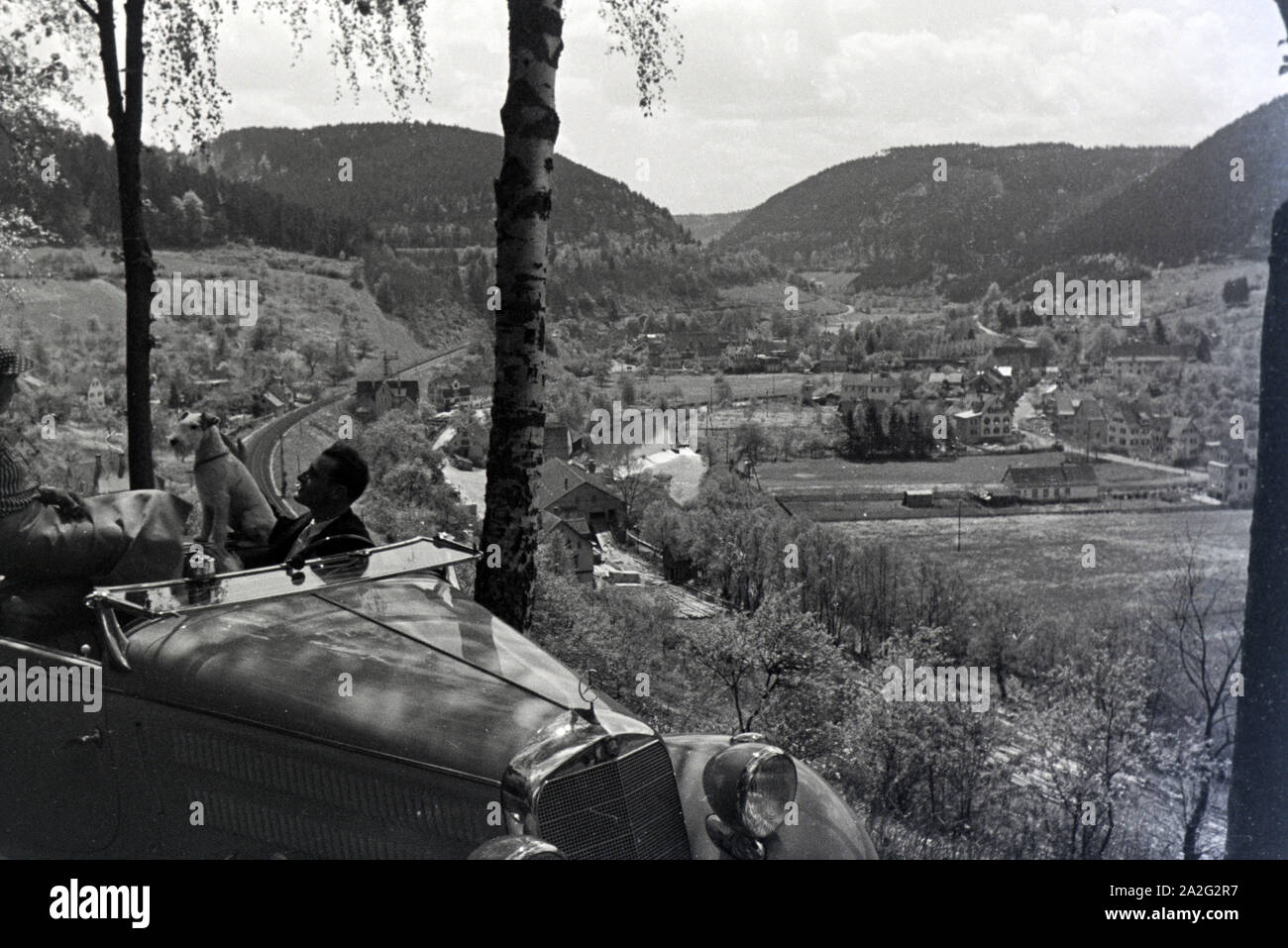 Ein junges Paar und ihr Hund bei einer Spazierfahrt mit dem Mercedes Cabrio in Hirsau im Nordschwarzwald, Deutschland 1930er Jahre. Ein junges Paar und ihr Hund fahren durch Hirsau im Nordschwarzwald in einem Mercedes Cabrio, Deutschland 1930. Stockfoto