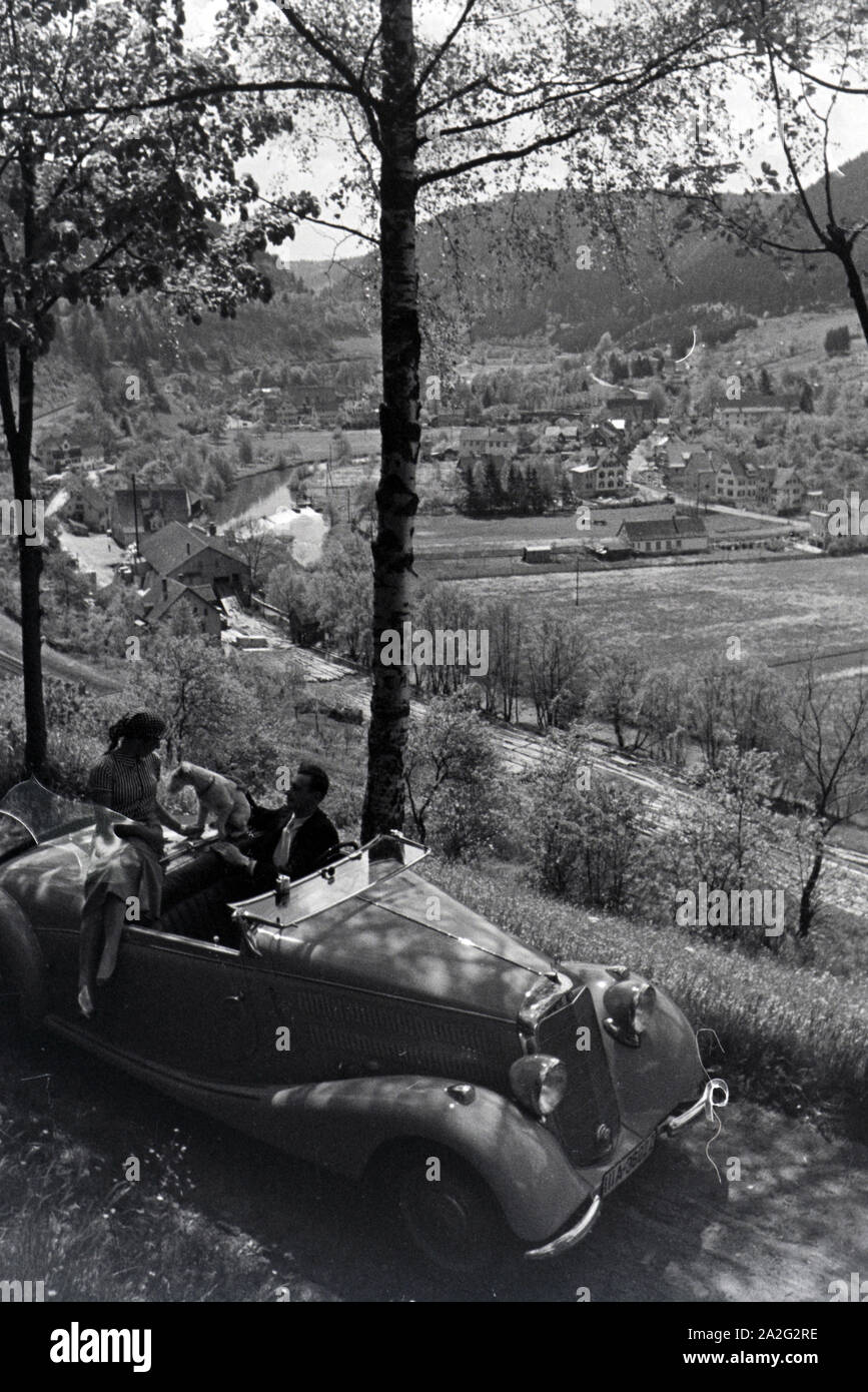 Ein junges Paar und ihr Hund bei einer Spazierfahrt mit dem Mercedes Cabrio in Hirsau im Nordschwarzwald, Deutschland 1930er Jahre. Ein junges Paar und ihr Hund fahren durch Hirsau im Nordschwarzwald in einem Mercedes Cabrio, Deutschland 1930. Stockfoto