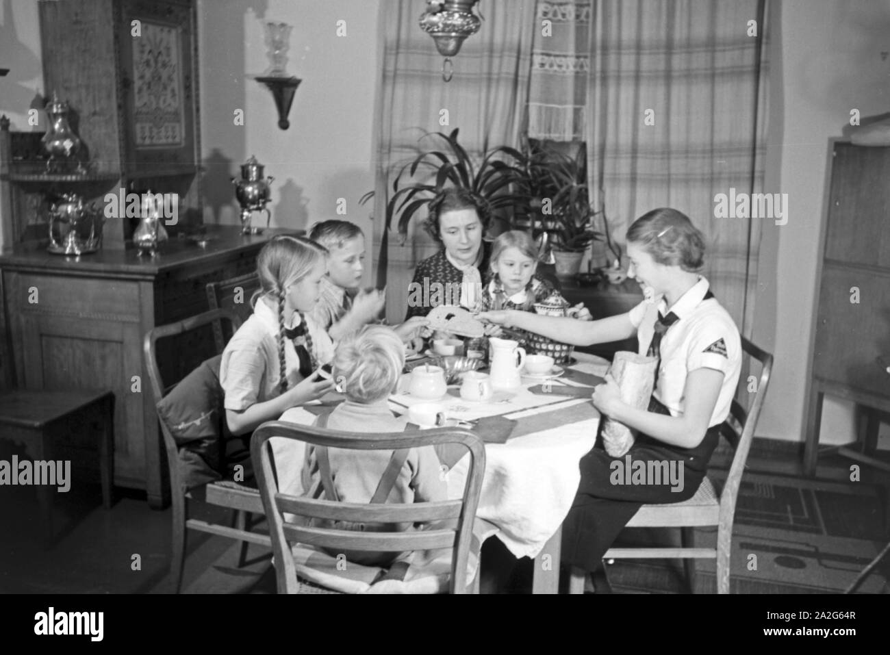 Eine Mutter sitzt mit fünf Kinder beim Frühstück am Küchentisch, Deutschland 1930er Jahre. Eine Mutter und ihre fünf Kinder mit Frühstück in der Küche, Deutschland 1930. Stockfoto