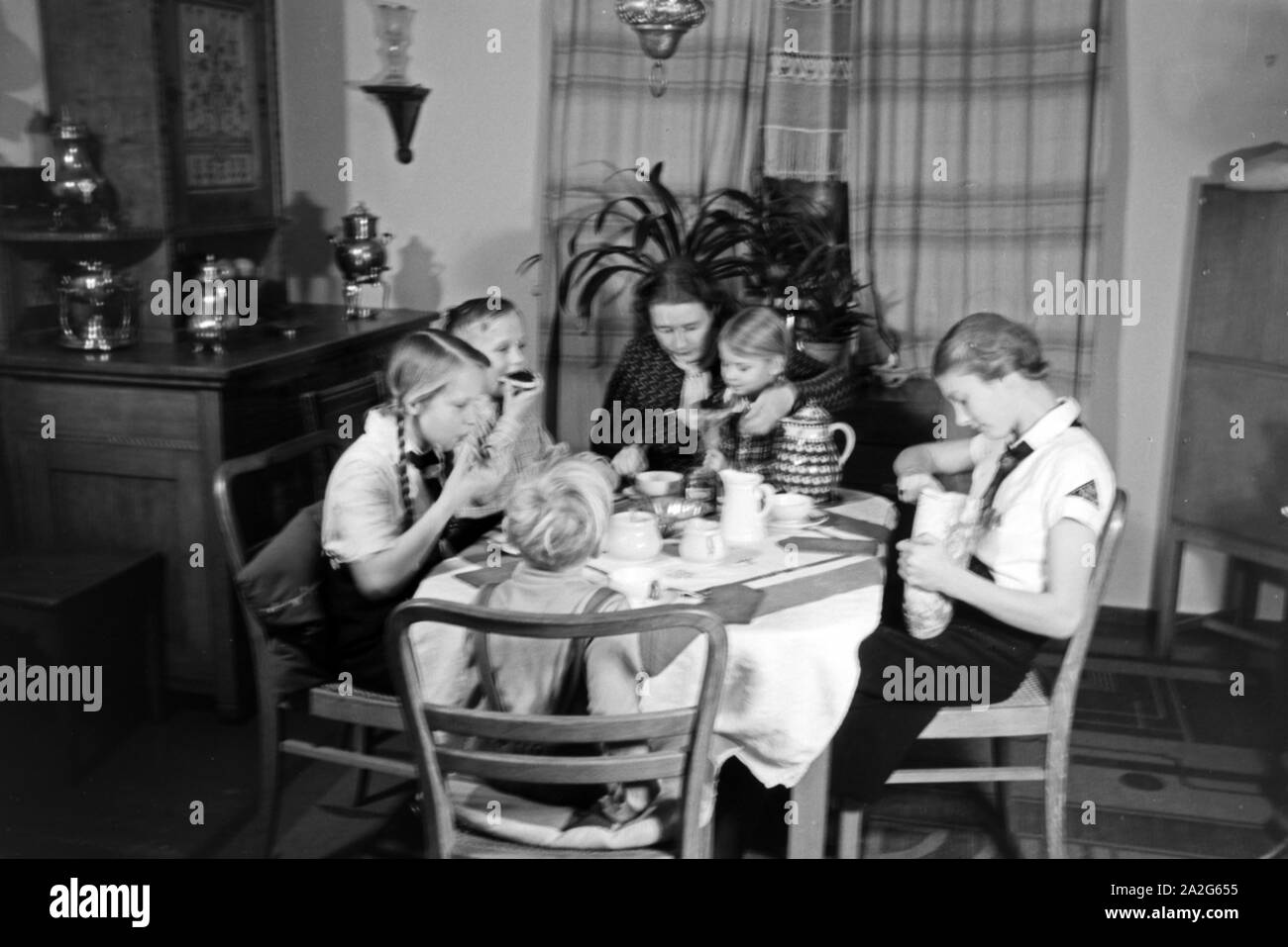 Eine Mutter sitzt mit fünf Kinder beim Frühstück am Küchentisch, Deutschland 1930er Jahre. Eine Mutter und ihre fünf Kinder mit Frühstück in der Küche, Deutschland 1930. Stockfoto