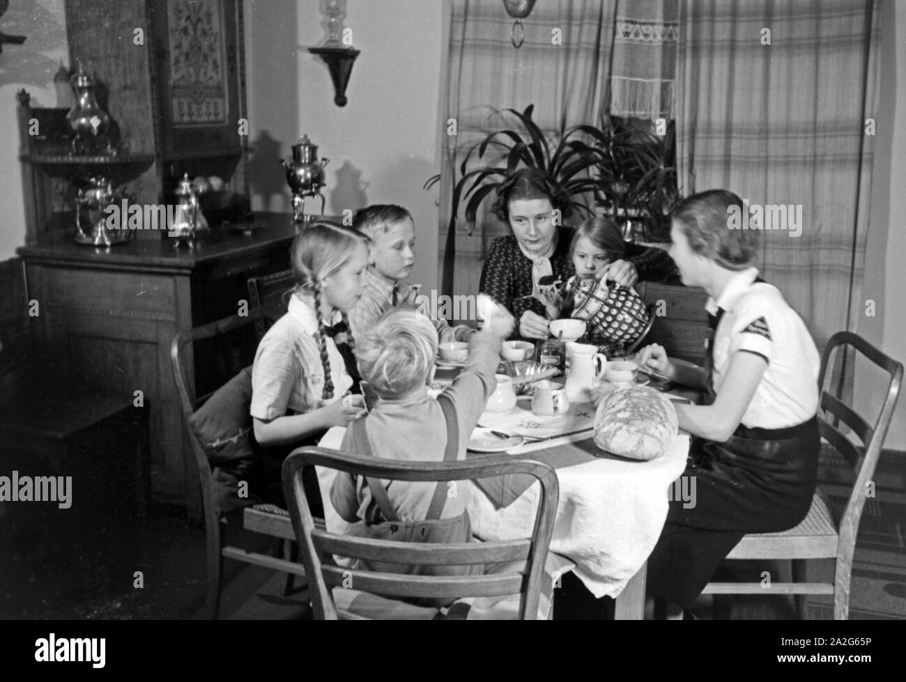 Eine Mutter sitzt mit fünf Kinder beim Frühstück am Küchentisch, Deutschland 1930er Jahre. Eine Mutter und ihre fünf Kinder mit Frühstück in der Küche, Deutschland 1930. Stockfoto