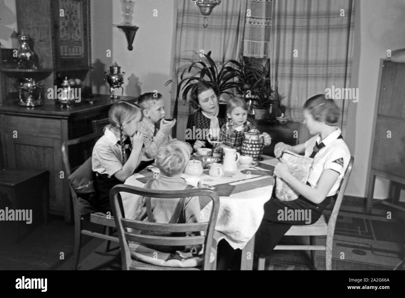 Eine Mutter sitzt mit fünf Kinder beim Frühstück am Küchentisch, Deutschland 1930er Jahre. Eine Mutter und ihre fünf Kinder mit Frühstück in der Küche, Deutschland 1930. Stockfoto