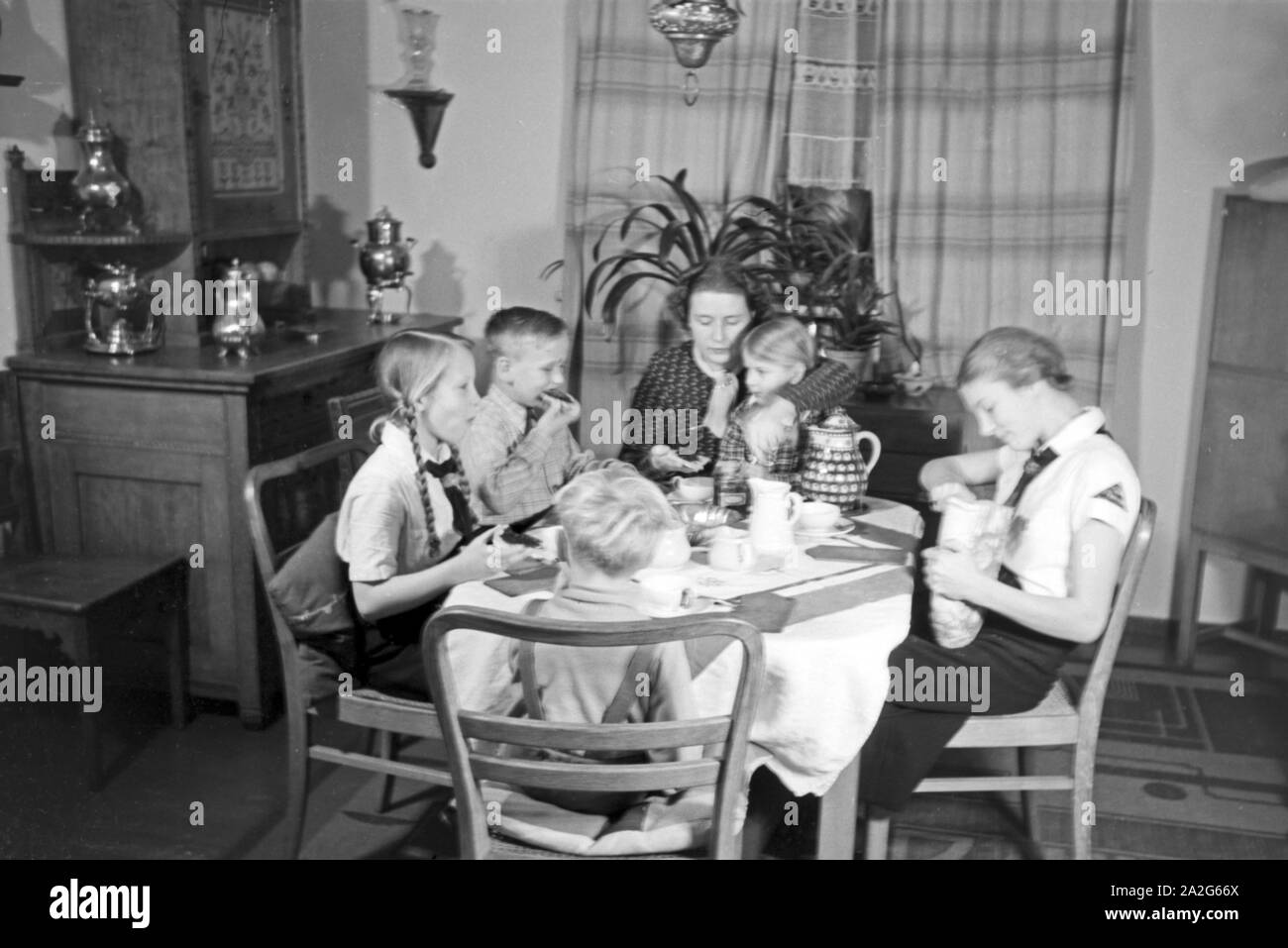 Eine Mutter sitzt mit fünf Kinder beim Frühstück am Küchentisch, Deutschland 1930er Jahre. Eine Mutter und ihre fünf Kinder mit Frühstück in der Küche, Deutschland 1930. Stockfoto