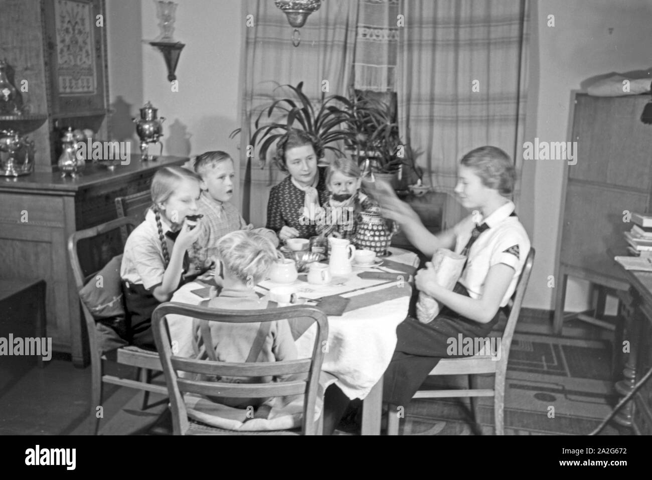 Eine Mutter sitzt mit fünf Kinder beim Frühstück am Küchentisch, Deutschland 1930er Jahre. Eine Mutter und ihre fünf Kinder mit Frühstück in der Küche, Deutschland 1930. Stockfoto