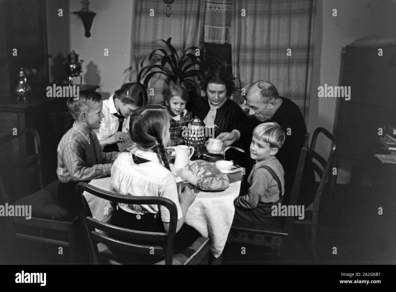 Ein Elternpaar sitzt mit fünf Kinder beim Frühstück am Küchentisch, Deutschland 1930er Jahre. Eltern und ihre fünf Kinder mit Frühstück in der Küche, Deutschland 1930. Stockfoto