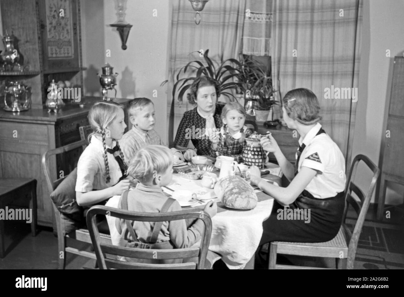 Eine Mutter sitzt mit fünf Kinder beim Frühstück am Küchentisch, Deutschland 1930er Jahre. Eine Mutter und ihre fünf Kinder mit Frühstück in der Küche, Deutschland 1930. Stockfoto