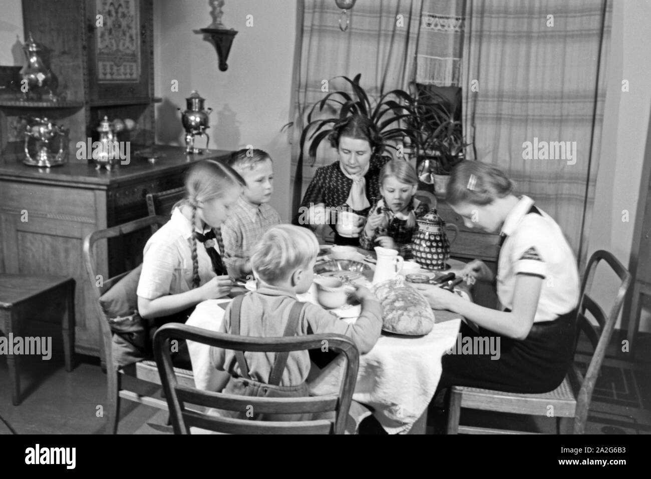 Eine Mutter sitzt mit fünf Kinder beim Frühstück am Küchentisch, Deutschland 1930er Jahre. Eine Mutter und ihre fünf Kinder mit Frühstück in der Küche, Deutschland 1930. Stockfoto
