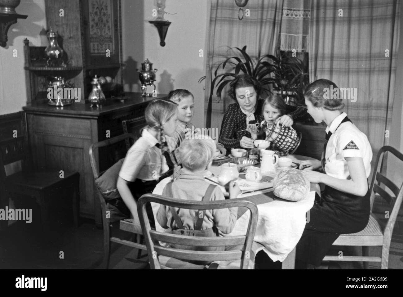 Eine Mutter sitzt mit fünf Kinder beim Frühstück am Küchentisch, Deutschland 1930er Jahre. Eine Mutter und ihre fünf Kinder mit Frühstück in der Küche, Deutschland 1930. Stockfoto