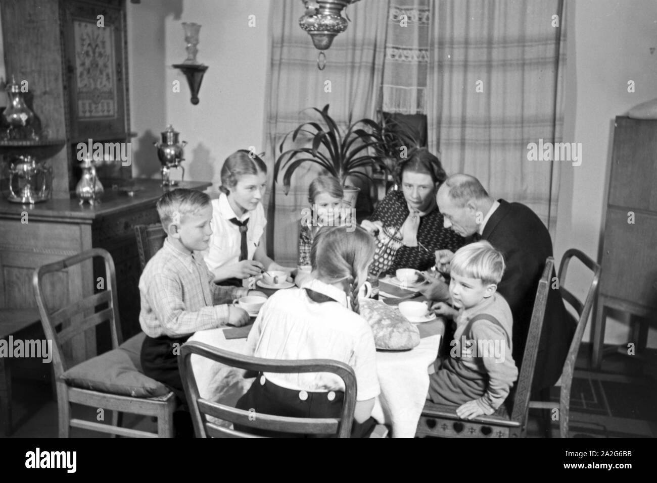 Ein Elternpaar sitzt mit fünf Kinder beim Frühstück am Küchentisch, Deutschland 1930er Jahre. Eltern und ihre fünf Kinder mit Frühstück in der Küche, Deutschland 1930. Stockfoto