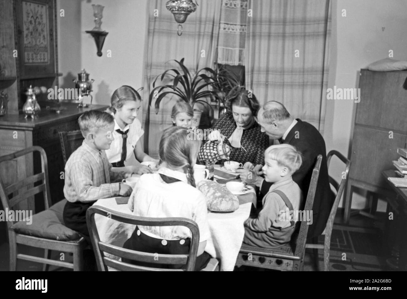 Ein Elternpaar sitzt mit fünf Kinder beim Frühstück am Küchentisch, Deutschland 1930er Jahre. Eltern und ihre fünf Kinder mit Frühstück in der Küche, Deutschland 1930. Stockfoto
