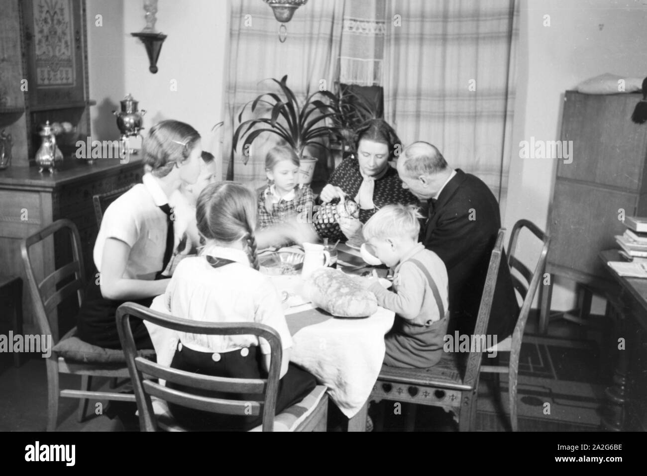 Ein Elternpaar sitzt mit fünf Kinder beim Frühstück am Küchentisch, Deutschland 1930er Jahre. Eine Mutter und ihre fünf Kinder mit Frühstück in der Küche, Deutschland 1930. Stockfoto