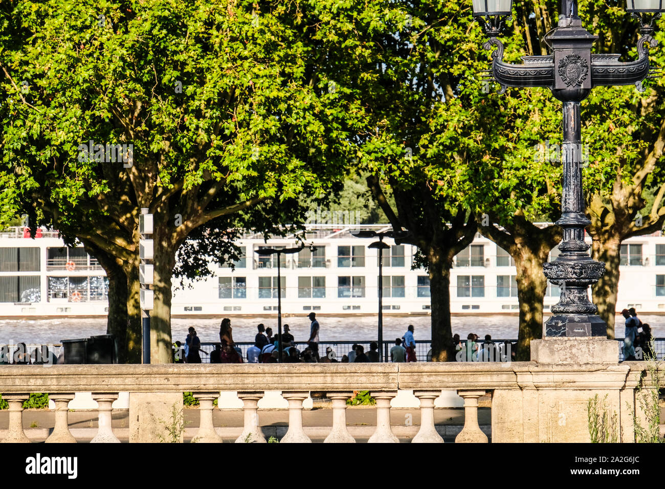 Leute sitzen auf Fluss Garonne Bank in Bordeaux, Frankreich, mit einem Fluss Kreuzfahrt Schiff durch gehend Stockfoto