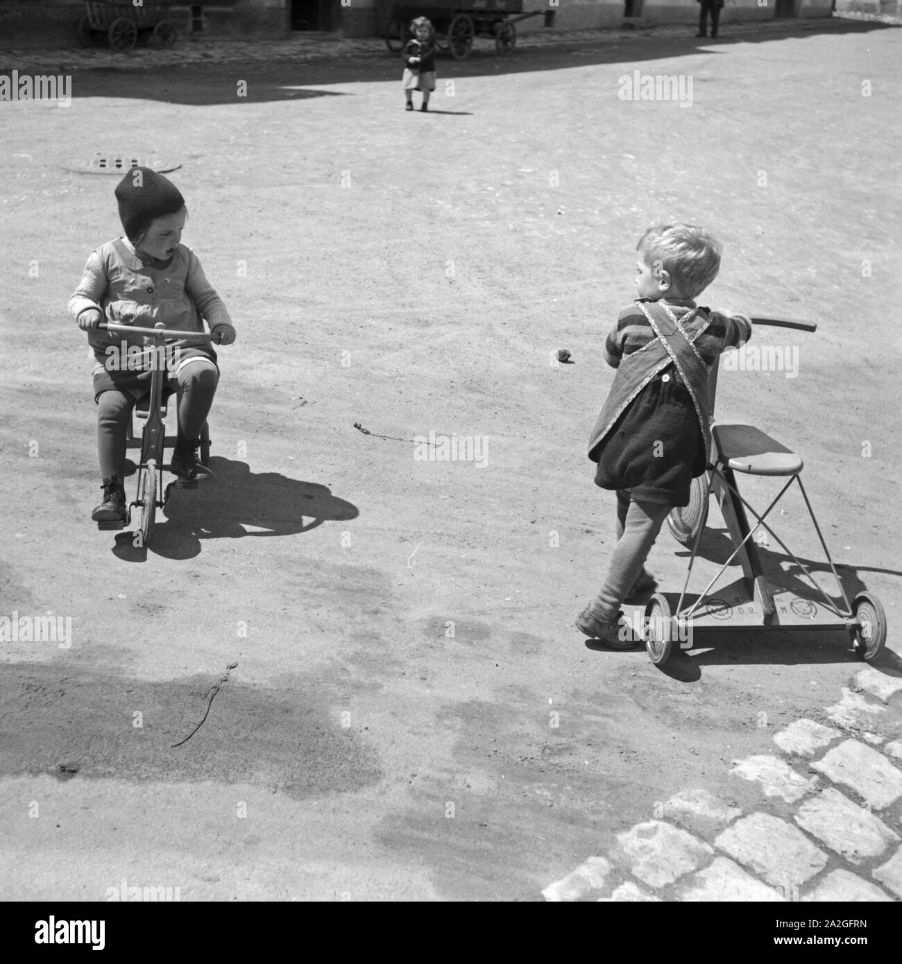 Zwei Kinder Spielen Mit Einem Dreirad, 1930er Jahre Deutschland. Zwei Kinder spielen mit einem Dreirad, Deutschland der 1930er Jahre. Stockfoto