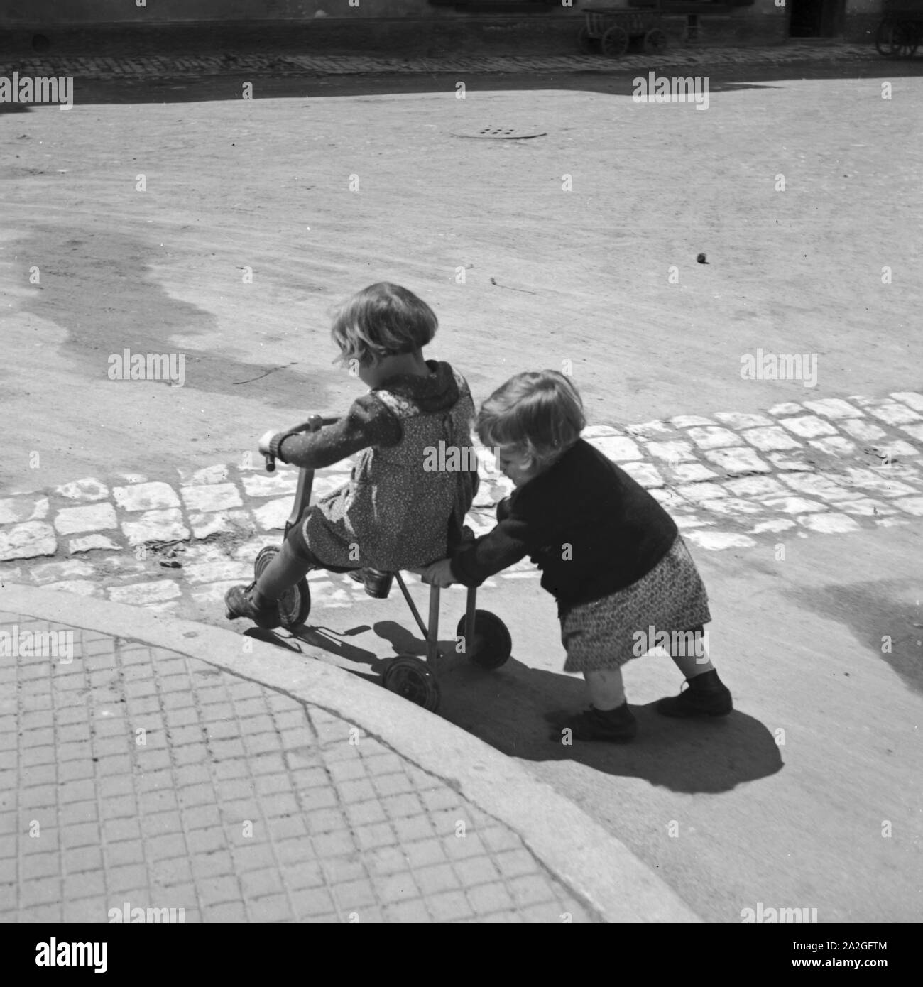 Zwei Kinder Spielen Mit Einem Dreirad, 1930er Jahre Deutschland. Zwei Kinder spielen mit einem Dreirad, Deutschland der 1930er Jahre. Stockfoto