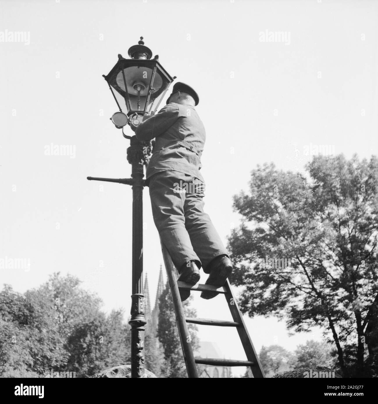 Ein Städtischer Bediensteter Wechselt Defekte Glühbirnen eine Einer Straßenlaterne aus, Deutschland 1930er Jahre. Ein Beamter, gebrochene Lampenwechsel von einer Straße Laterne, Deutschland der 1930er Jahre. Stockfoto