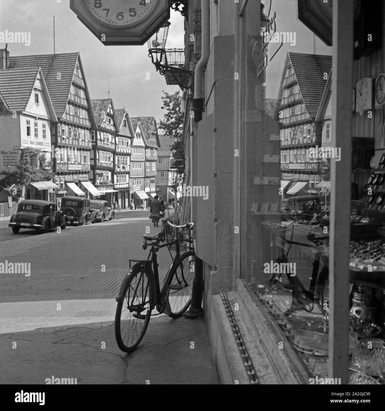 Häuser und eine Straße spiegeln sich im-Schaufenster eines Uhren- und Haushaltwarengeschäfts in Bad Wildungen, Deutschland 1930er Jahre. Häuser und eine Straße in das Fenster einer Uhr und Haushalt hardware Shop in Bad Wildungen, Deutschland der 1930er Jahre widerspiegelt. Stockfoto