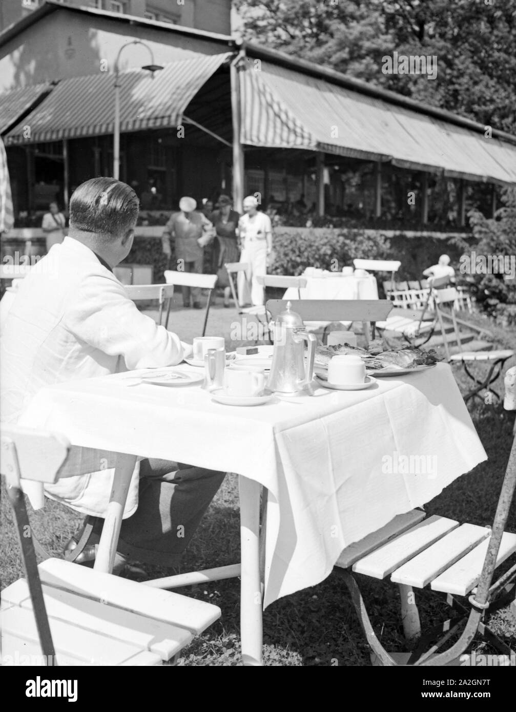 Ein Mann sitzt in der Außengastronomie im Garten eines Restaurants und wartet auf den Kellner, Deutschland 1930er Jahre. Ein Mann sitzt in der open air Gastronomie, warten auf einen Kellner, Deutschland 1930. Stockfoto