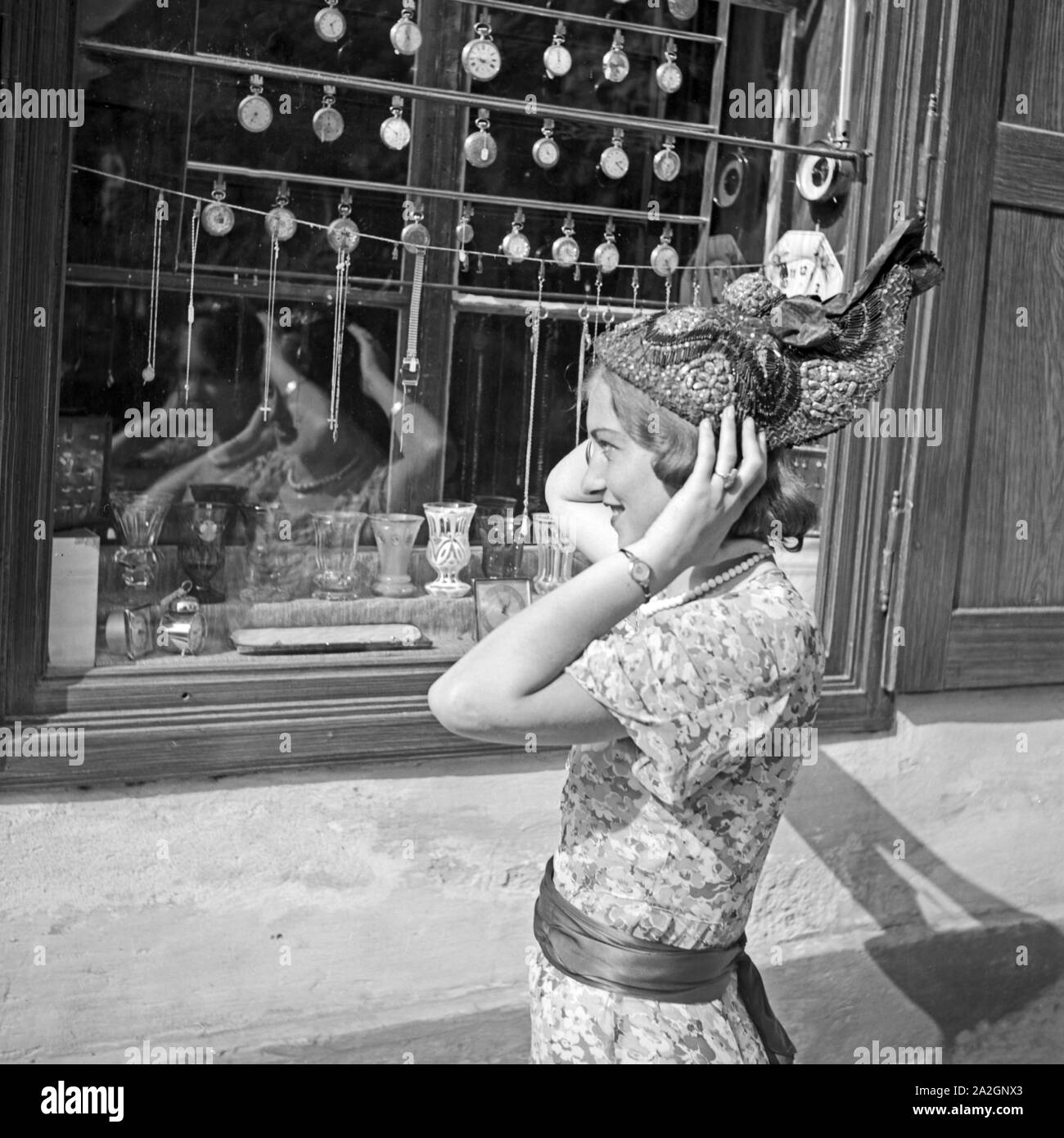 Eine junge Frau hat einen neuen Hut Referenzen und sieht in sich in der Spiegelung eines Schaufensters ein, Österreich 1930er Jahre. Eine junge Frau kaufte einen neuen Hut und prüft sie im Spiegel der ein Schaufenster, Österreich 1930. Stockfoto