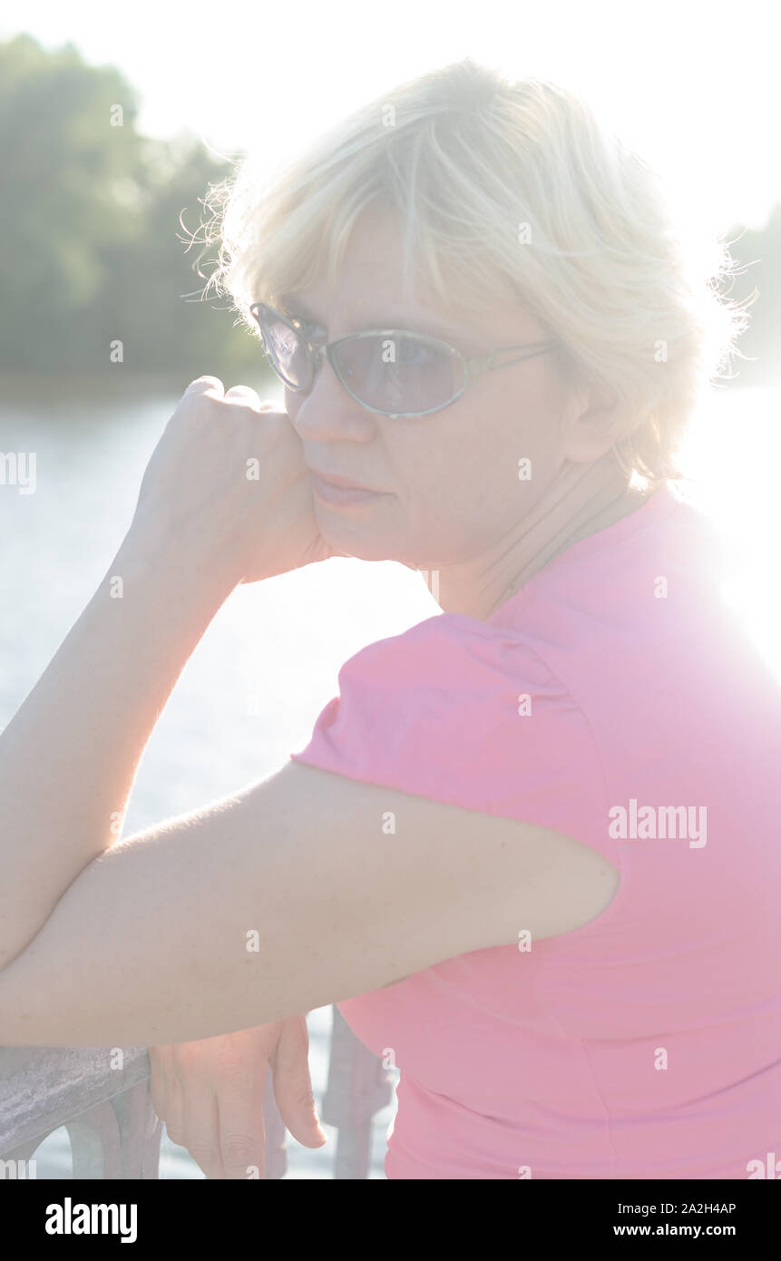 Eine Frau von 45-50 Jahre alt sitzt mit Traurigkeit in der Nähe des Flusses auf dem Damm Straße Stockfoto