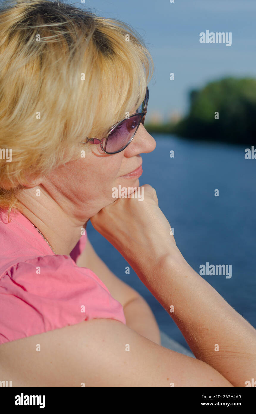 Eine Frau von 45-50 Jahre alt sitzt mit Traurigkeit in der Nähe des Flusses auf dem Damm Straße Stockfoto